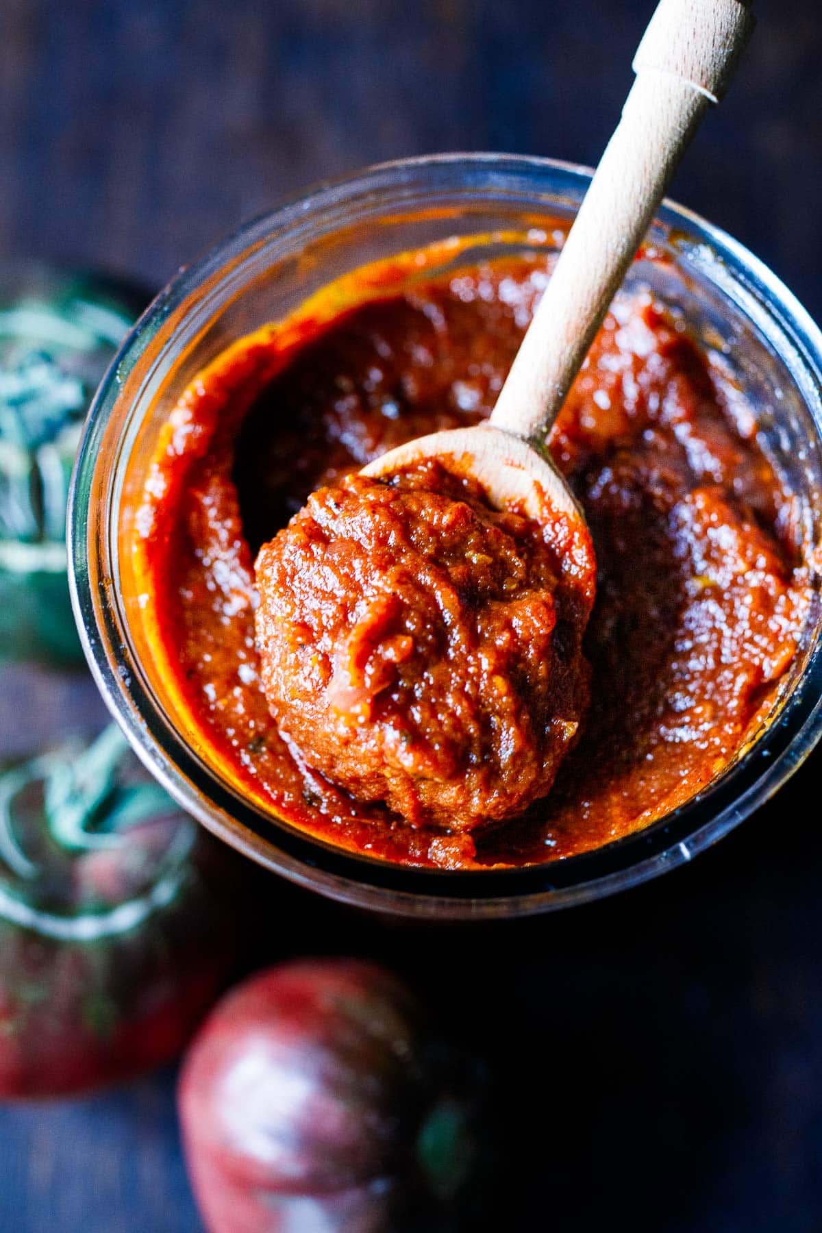 wooden spoon lifting up homemade ketchup from a jar.