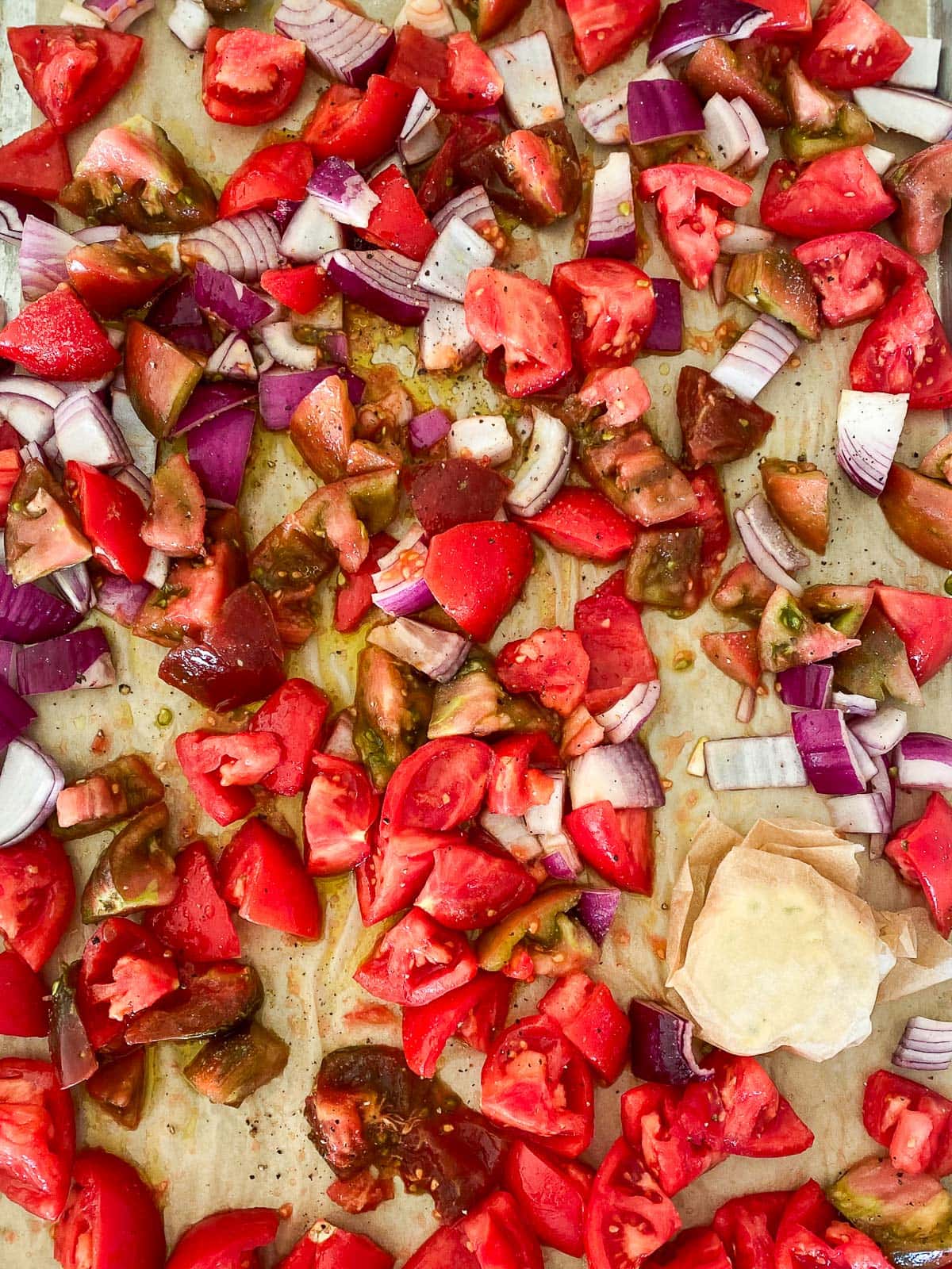 parchment lined baking sheet with chopped tomatoes and onion and parchment wrapped garlic head.