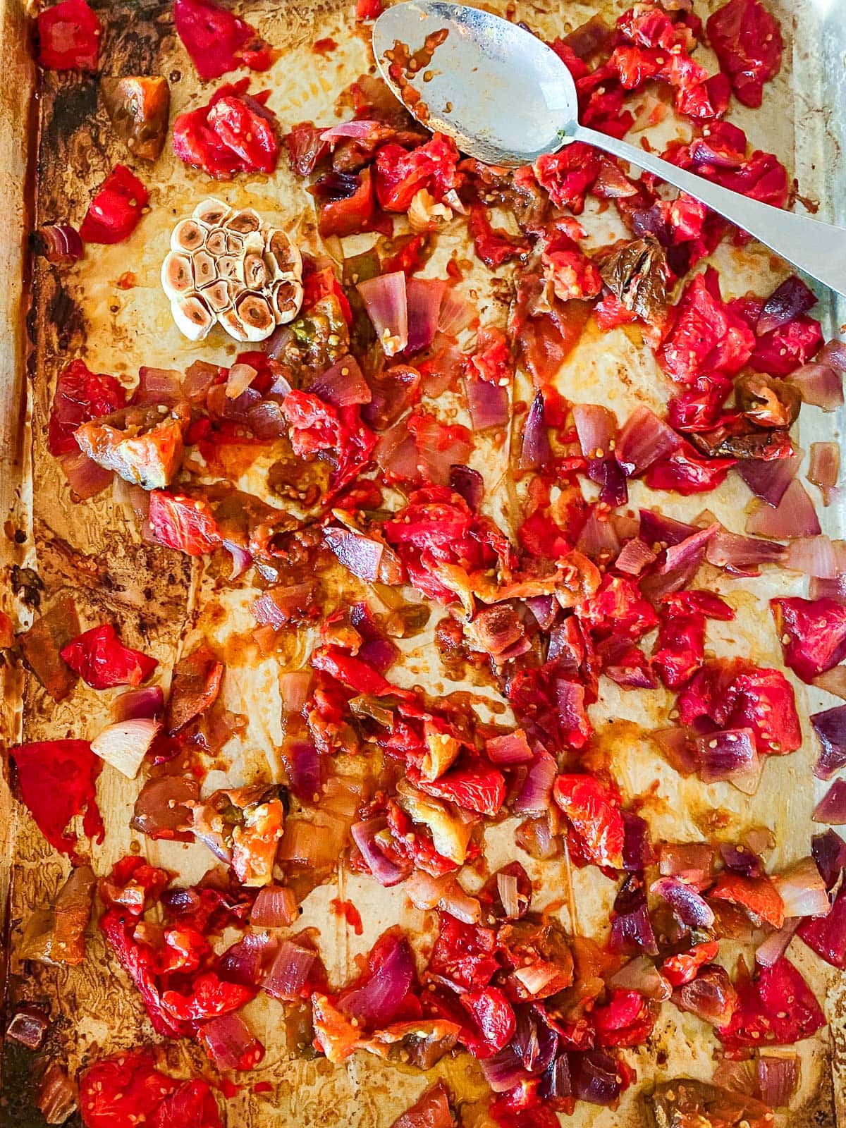 parchment-lined baking sheet with roasted tomatoes, onions, and garlic head.