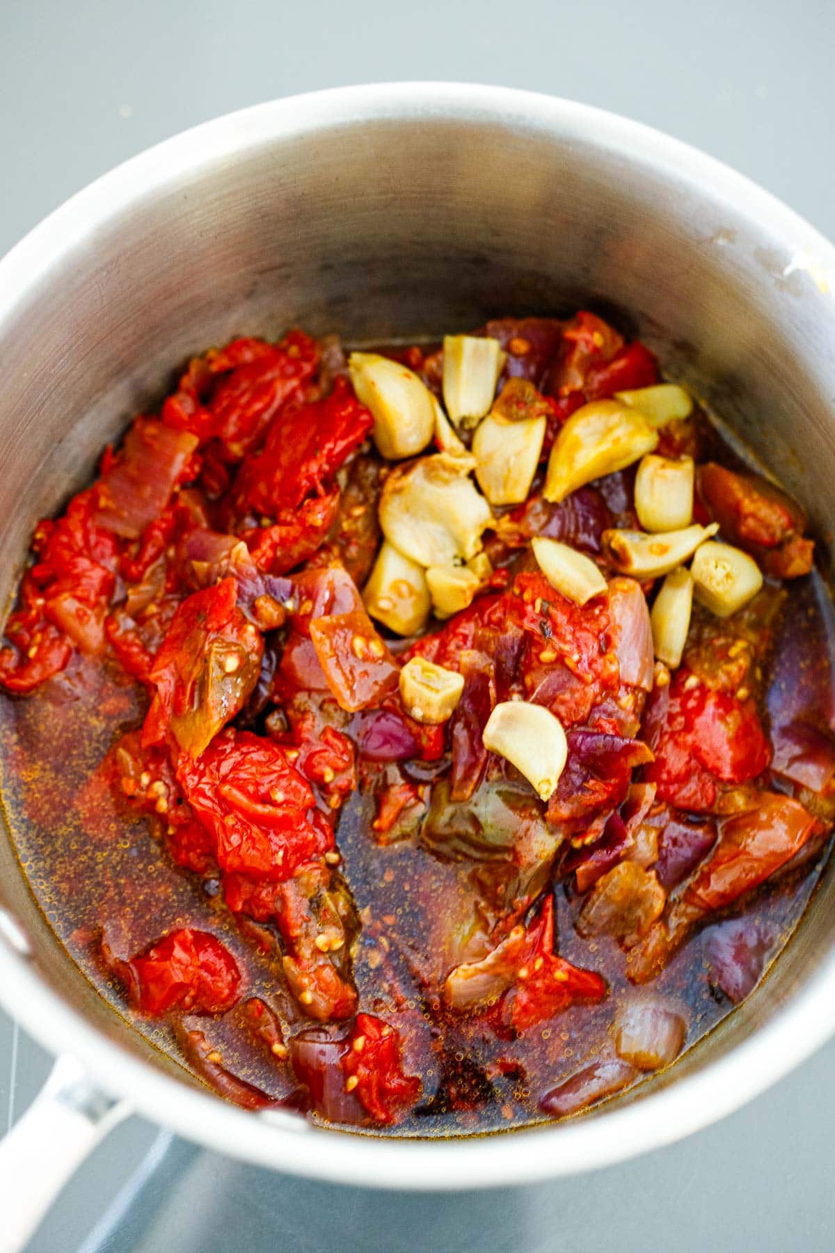 pot with roasted tomato onion mixture, roasted garlic cloves, and remaining ingredients for homemade ketchup.