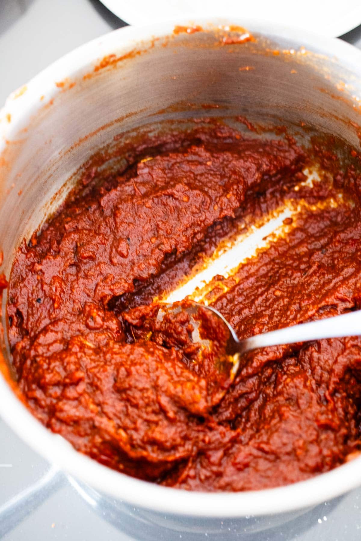 spoon stirring thickened homemade ketchup in pot.