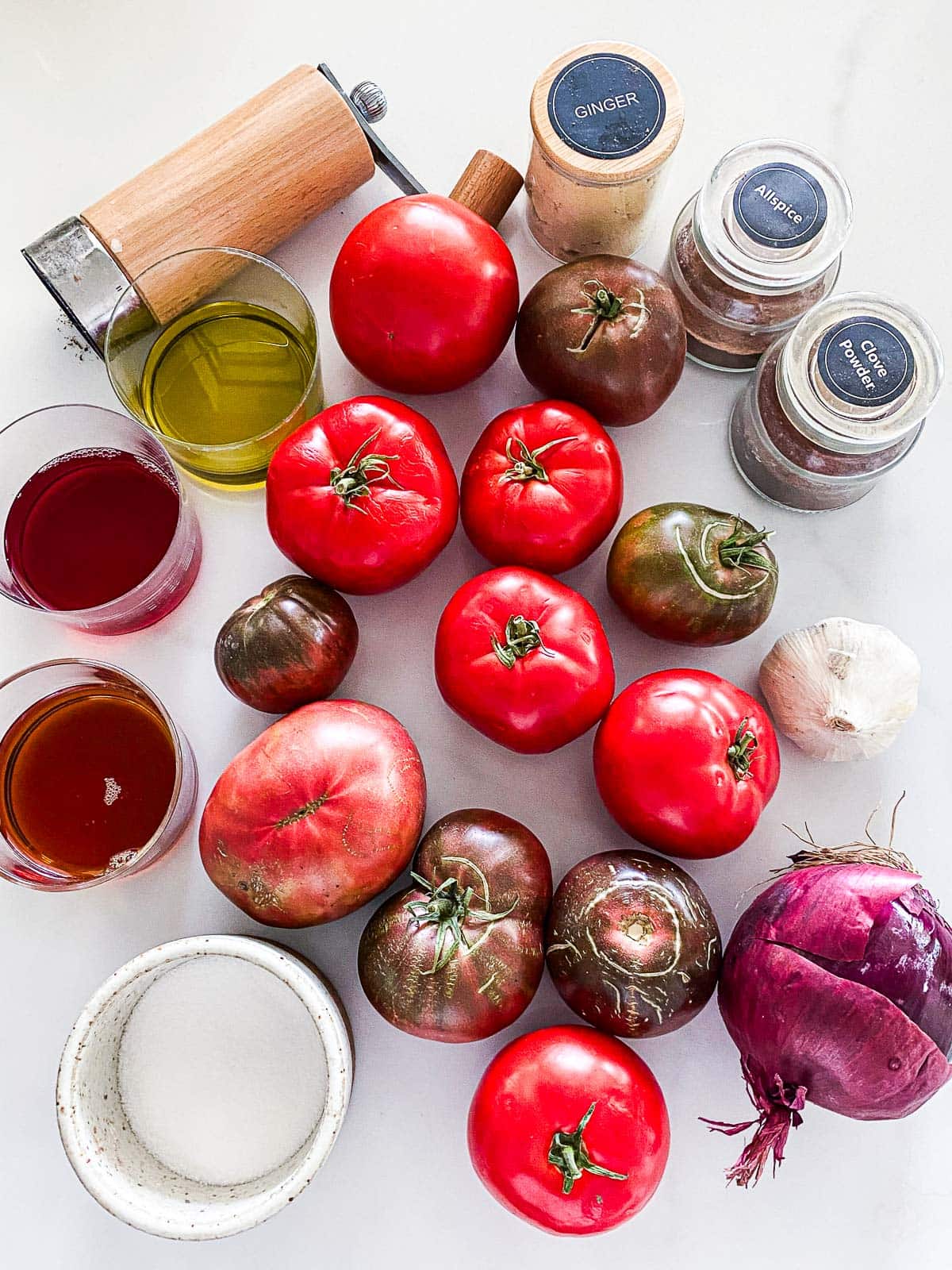 ingredients laid out for making homemade ketchup - spices, tomatoes, vinegar, syrup, salt, onion, garlic.