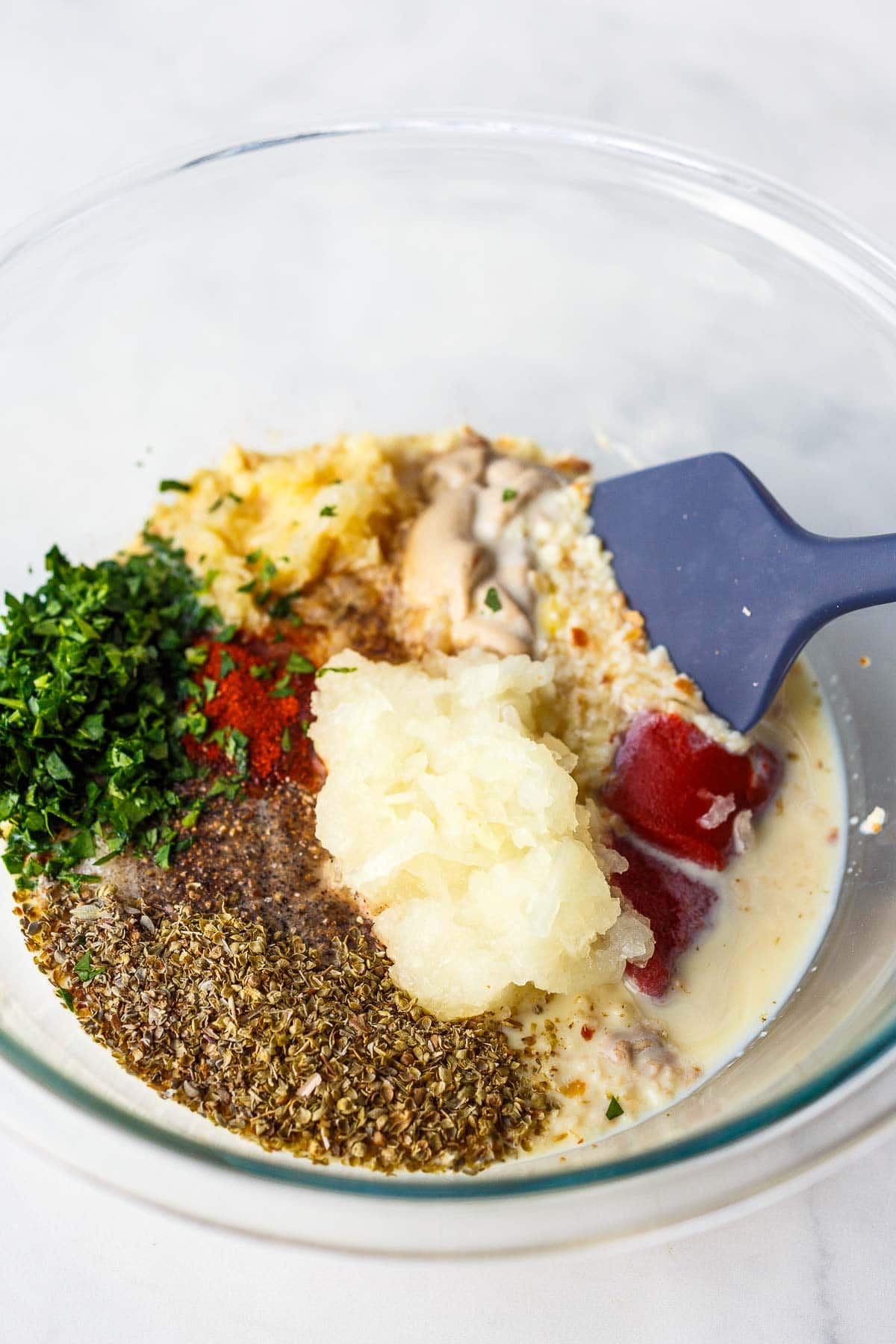 mixing bowl with grated onion and garlic, tomato paste, mustard, parsley, spices, and remaining ingredients with spatula to mix. 