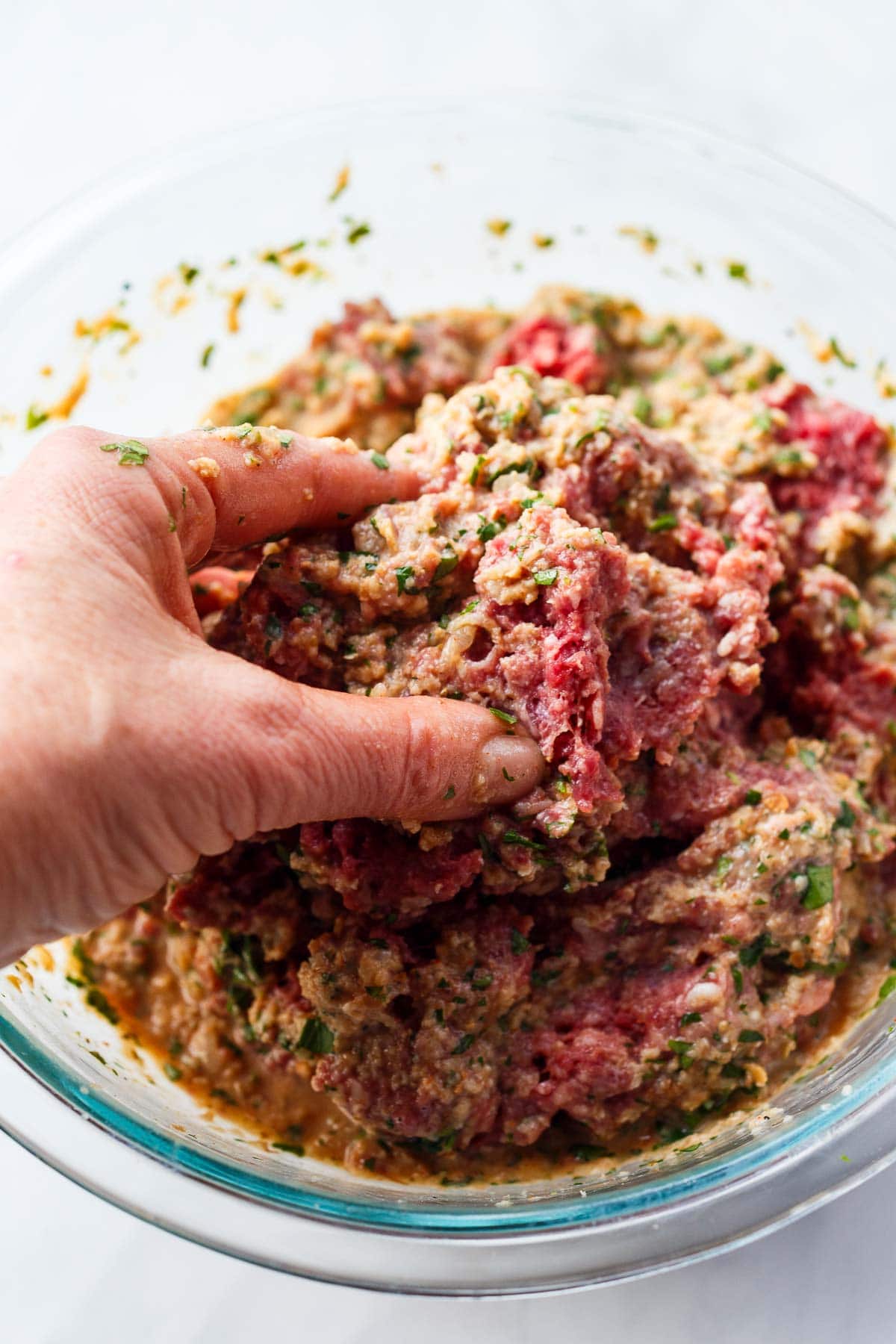 hands mixing ground beef into mixing bowl with remaining ingredients. 