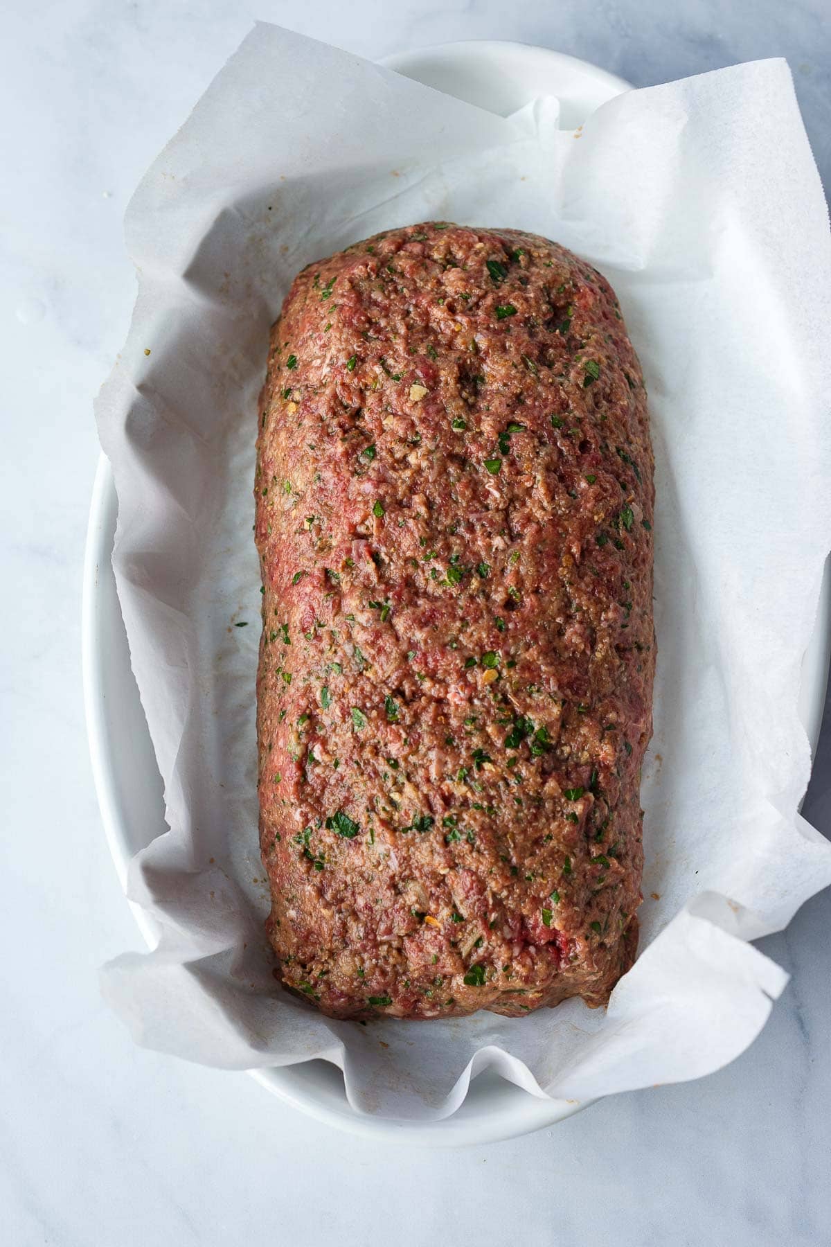 ground beef mixture formed into loaf shape on parchment-lined oval baking dish.