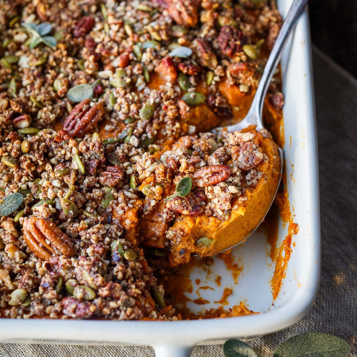 serving spoon lifting up sweet potato casserole with pecan crumble topping.