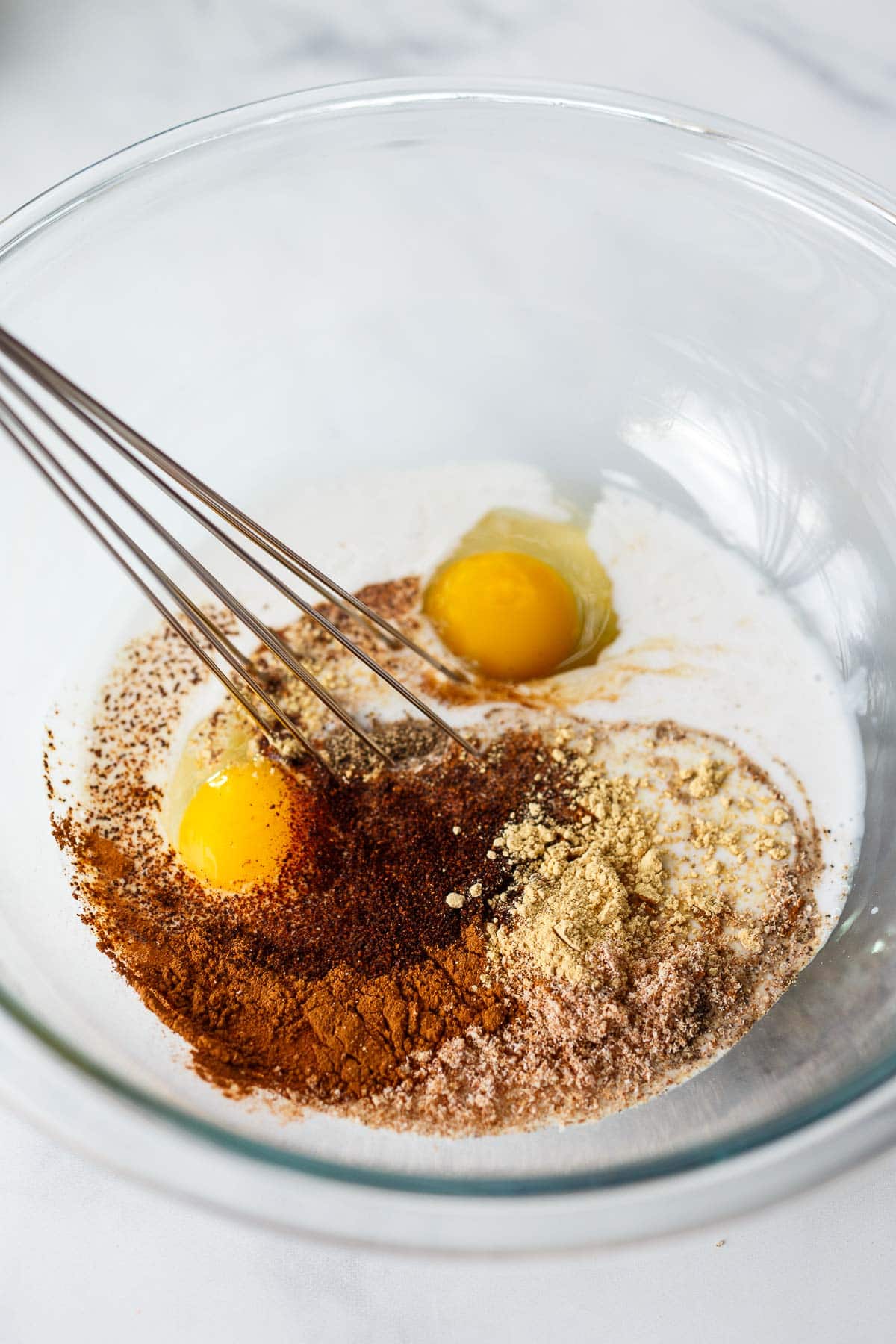 glass mixing bowl with eggs, spices, and coconut milk.