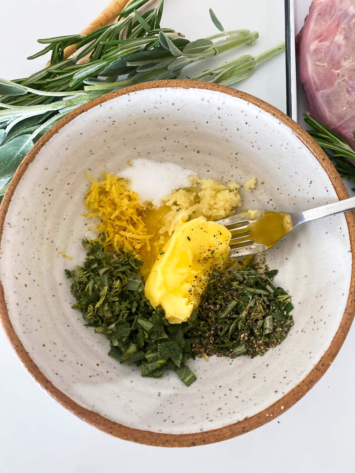 small bowl with butter, herbs, garlic, lemon, salt, and pepper, and fork.
