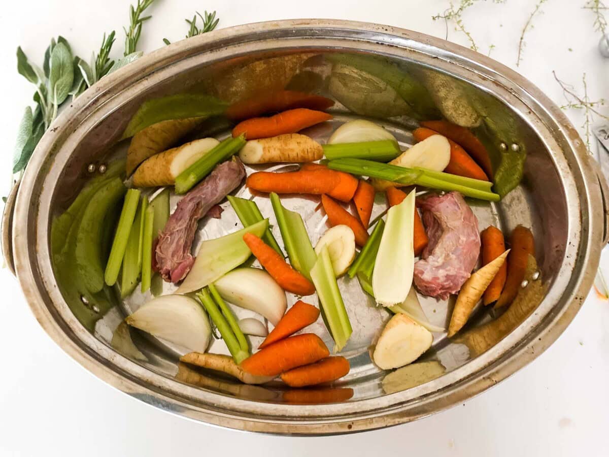 oval roasting pan with cut vegetables and turkey neck cut in two.