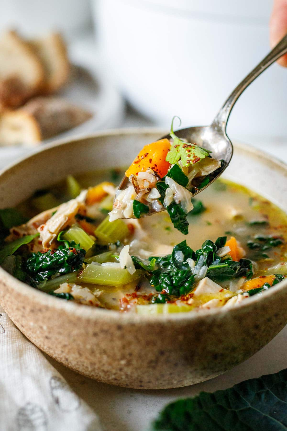 bowl of turkey rice soup with spoon lifting a spoonful up with carrots, parsley, and rice.