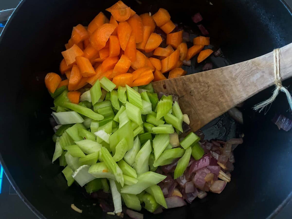 large pot with chopped carrots and celery added to cooked onions.