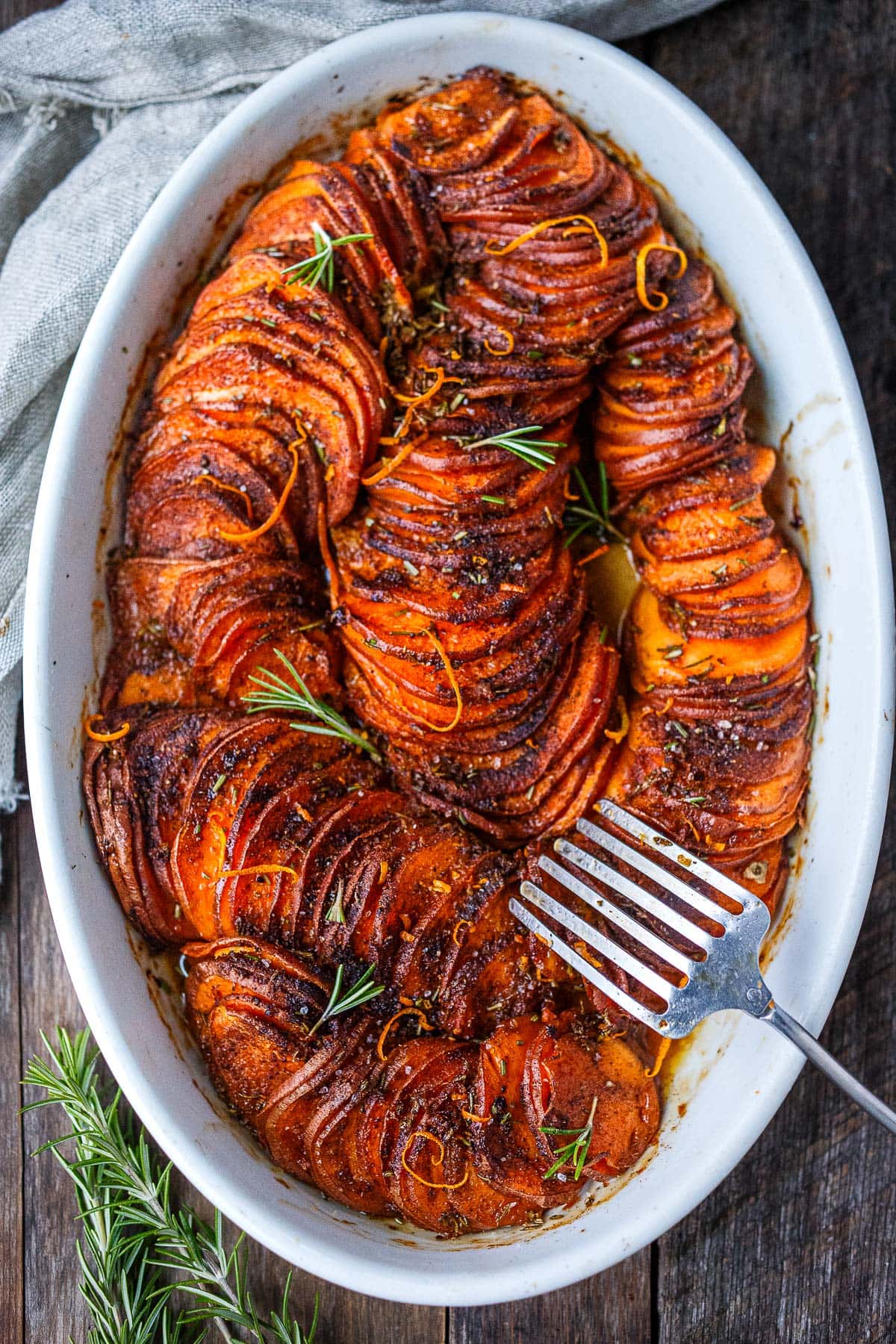 oval baking dish with serving fork with vegan sweet potato casserole with sliced yams in spiral pattern. 