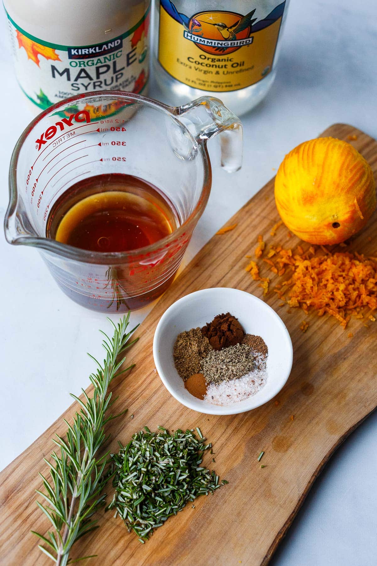 small bowl with spices on wood board with zested orange and minced rosemary. 