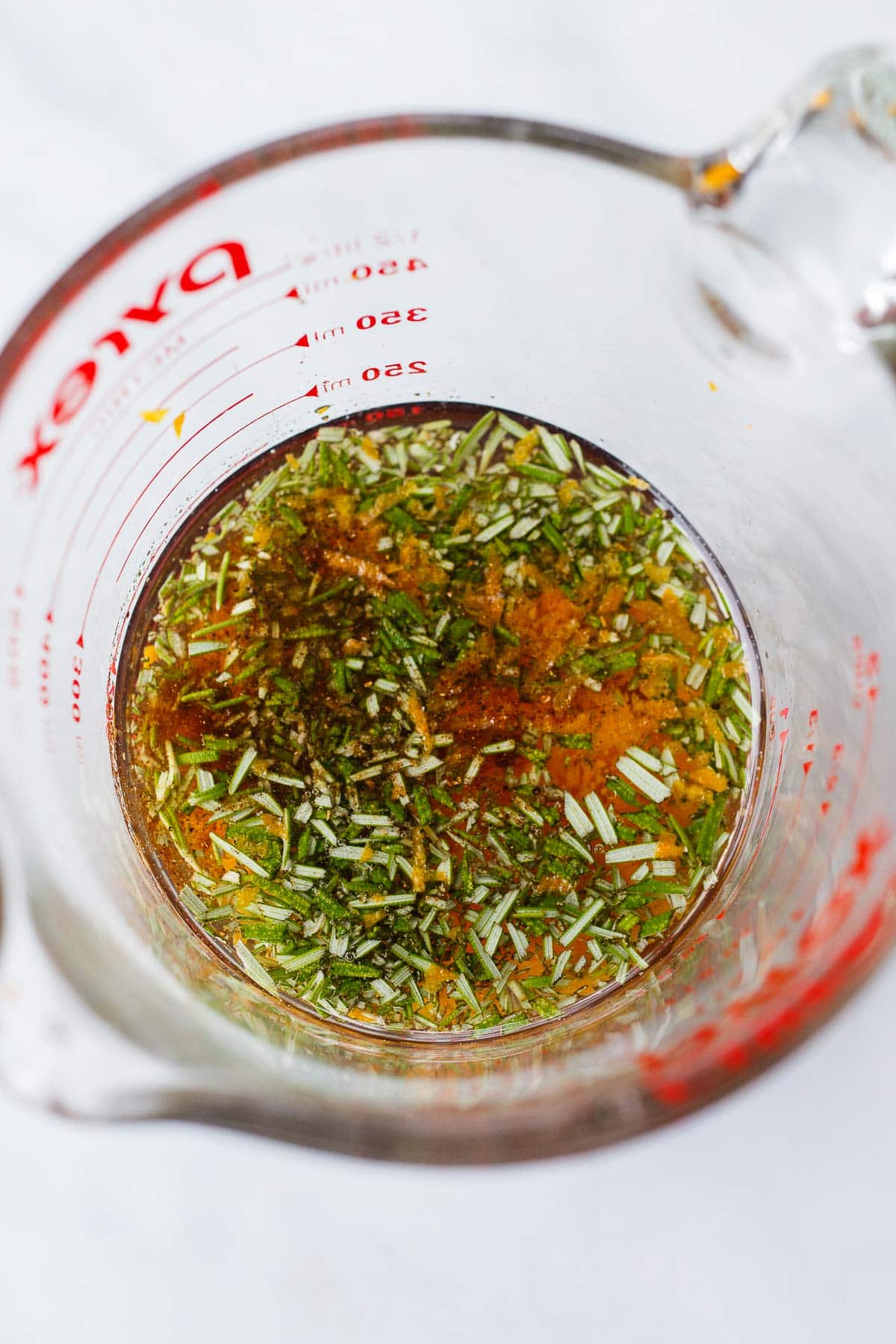 measuring cup with melted coconut oil and minced herbs and orange zest and spices. 