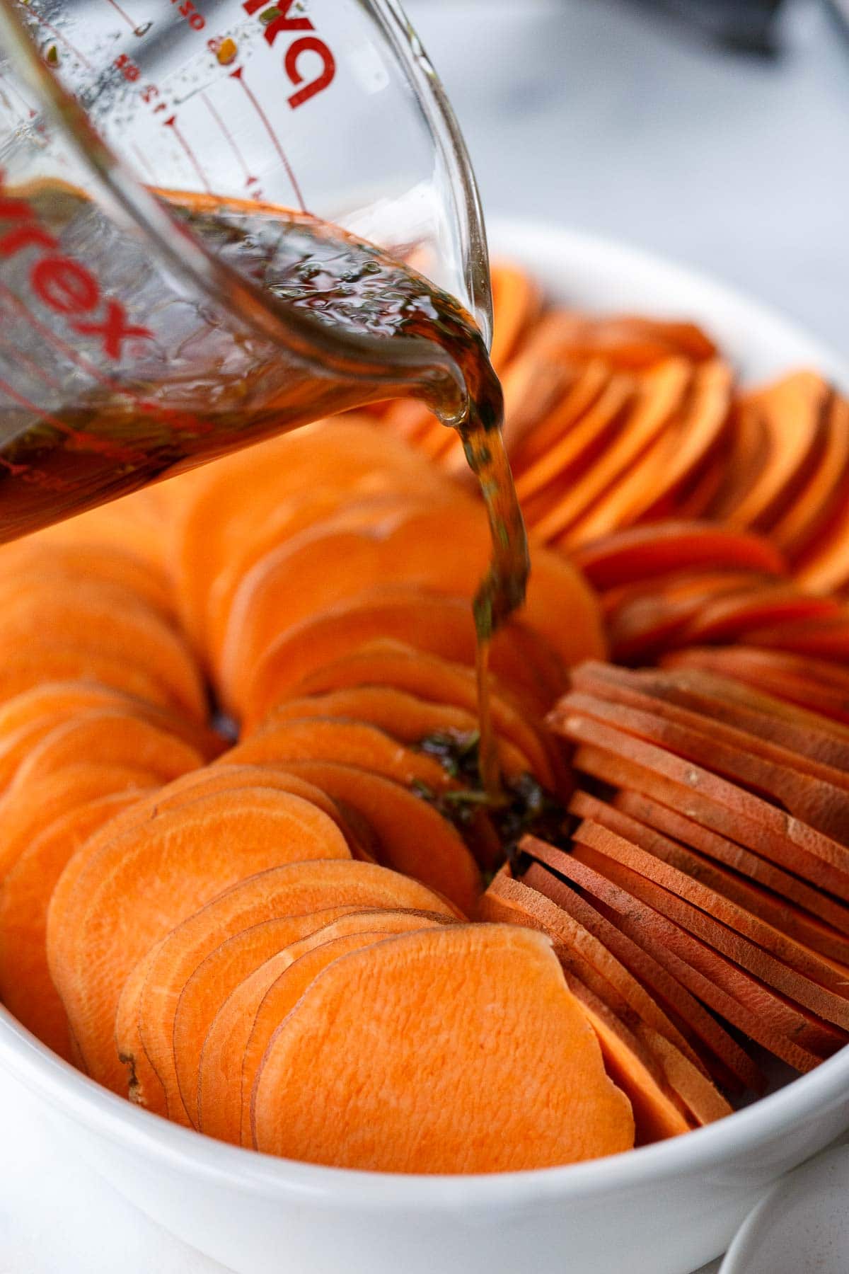 pouring orange coconut oil mixture over top of sliced yams in baking dish. 