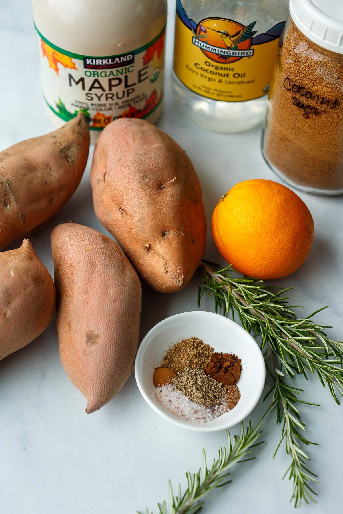 ingredients for vegan sweet potato casserole - maple syrup, coconut oil, coconut sugar, sweet potatoes, orange, rosemary, spices. 
