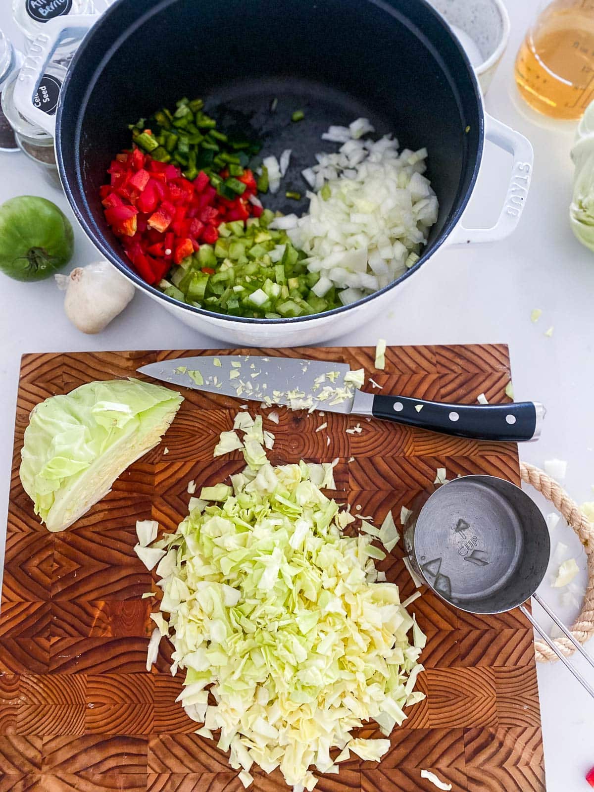 wood board and knife with chopped cabbage next to pot with other chopped veggies for chow chow. 