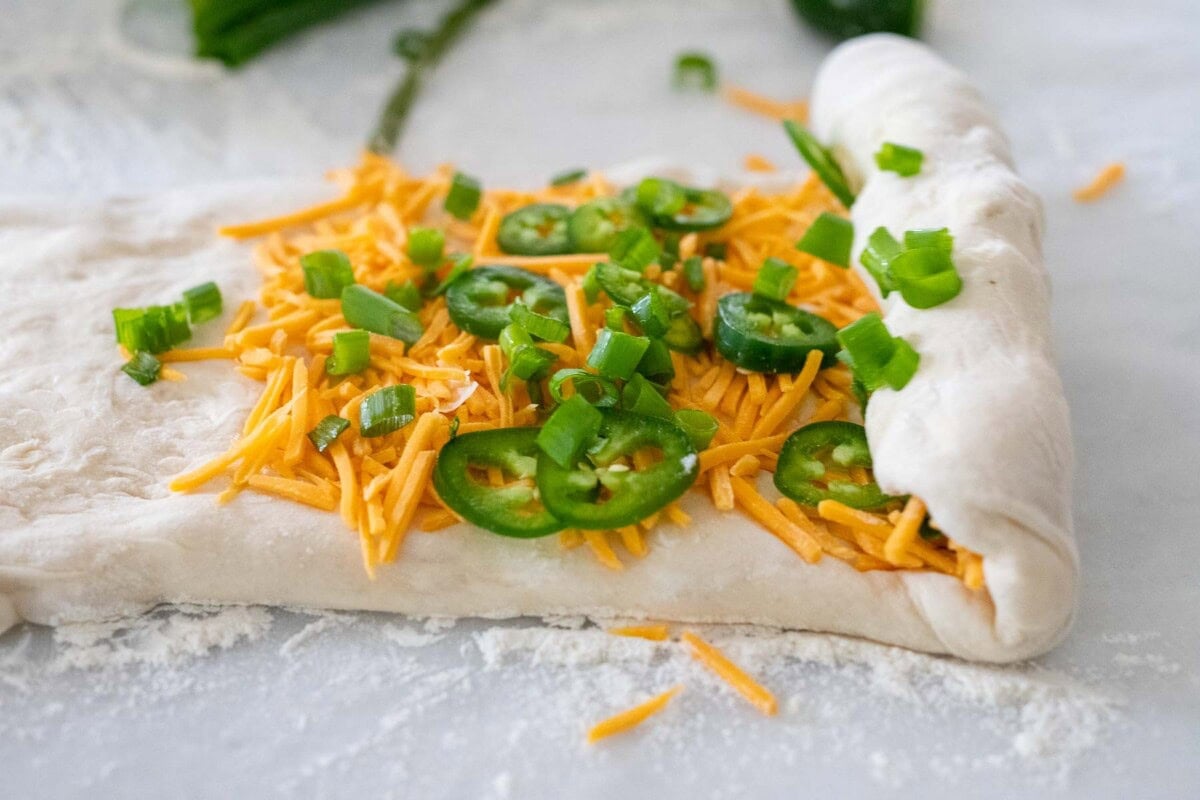 rolling the dough toward the center with the cheddar and jalapeno on the inside.