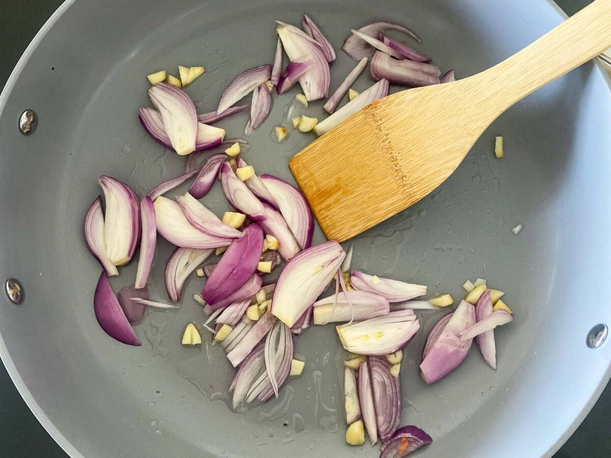 skillet with shallots and garlic cloves and wood spatula. 