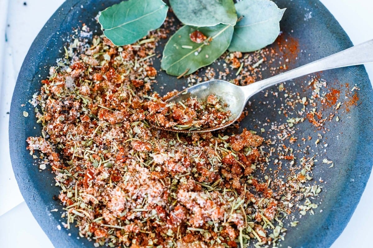 spoon mixing together spices for spice rub with bay leaves off to the side. 