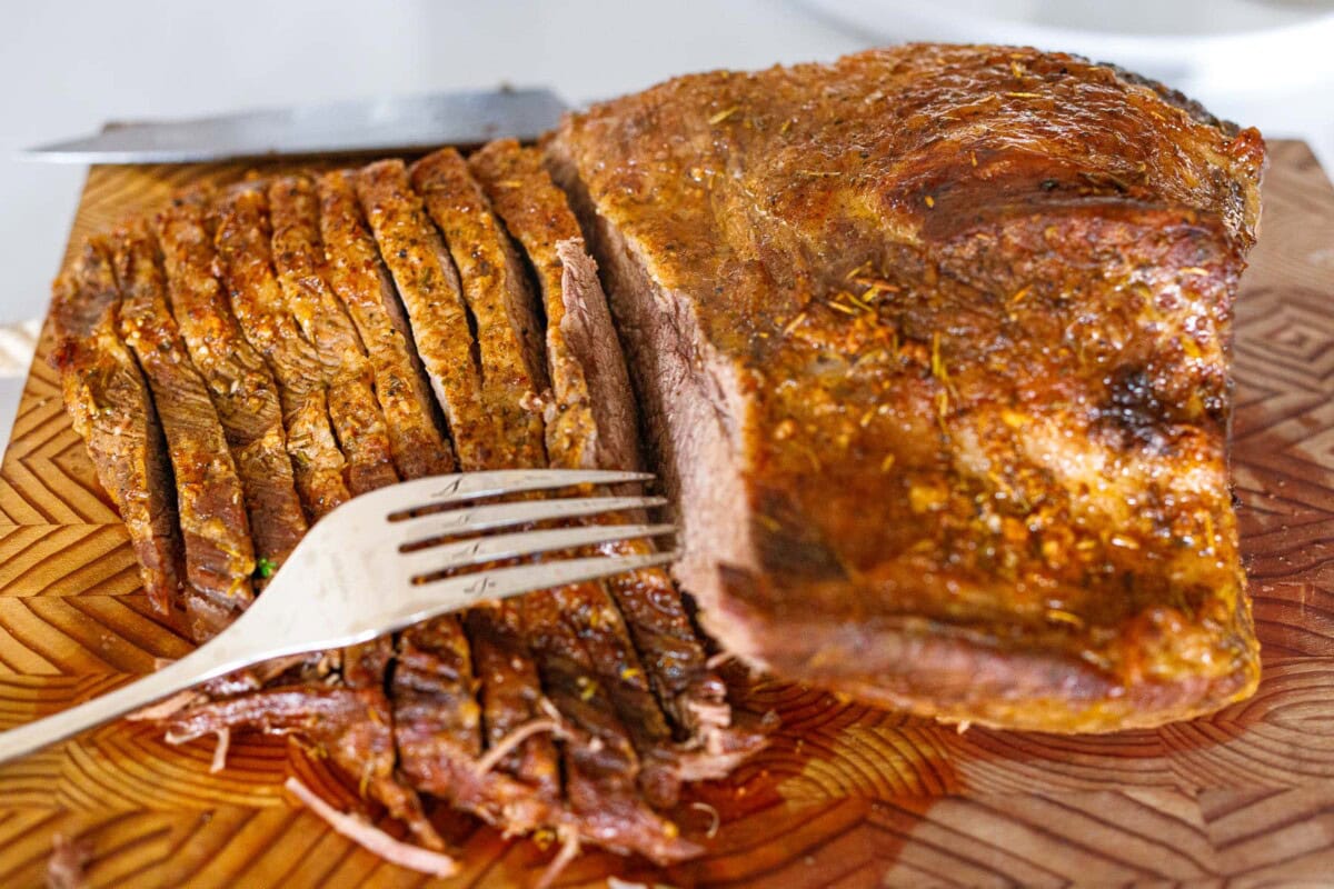 beef brisket with half of it sliced with fork pulling away the pieces. 