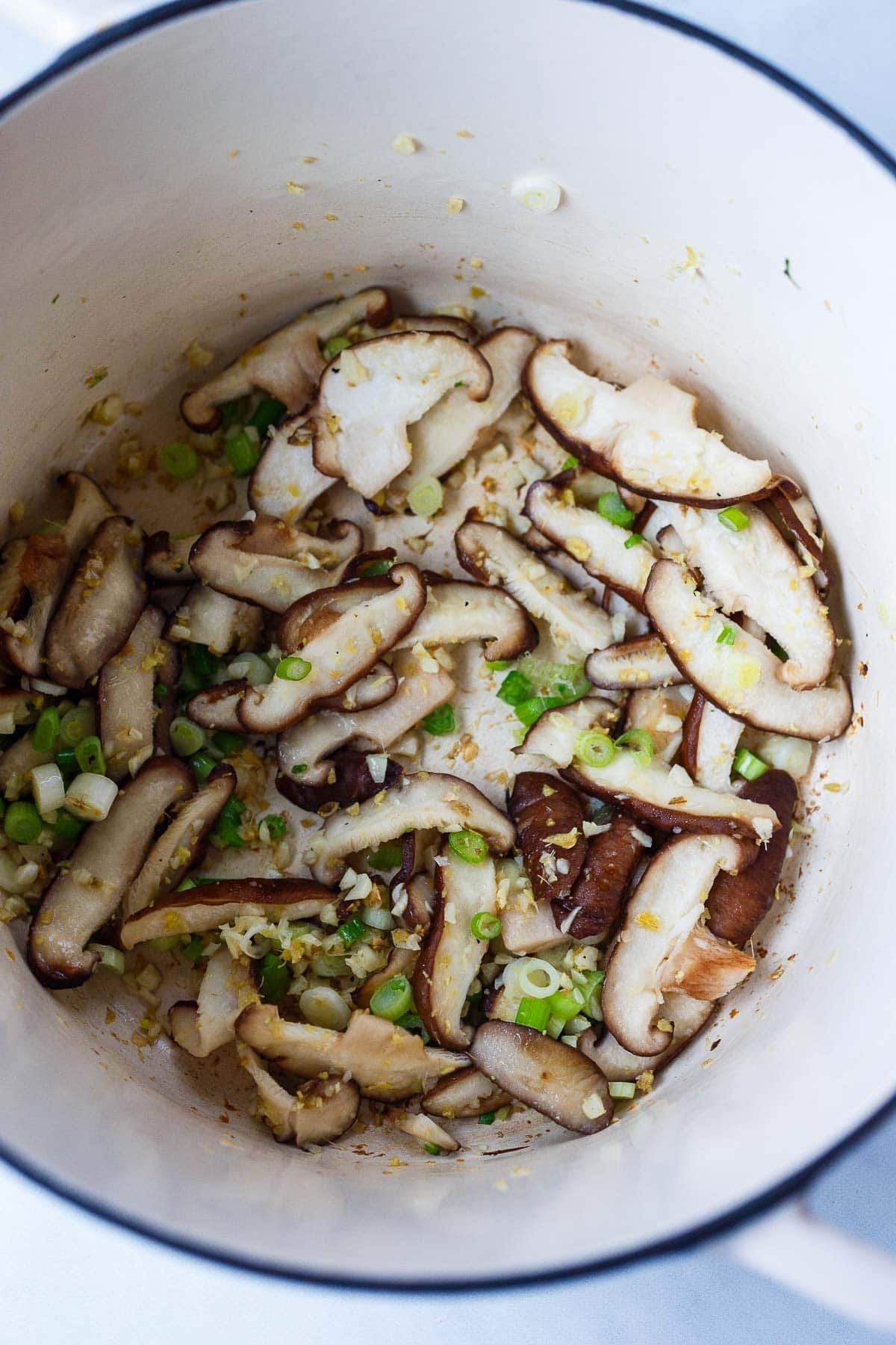 sliced shiitake mushrooms sautéing in pot with ginger, garlic, and scallions.