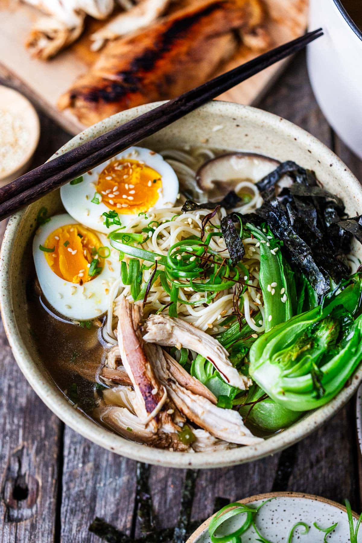 bowl of chicken ramen with bok choy, nori, shiitake, and boiled eggs, with chopsticks on top of bowl.