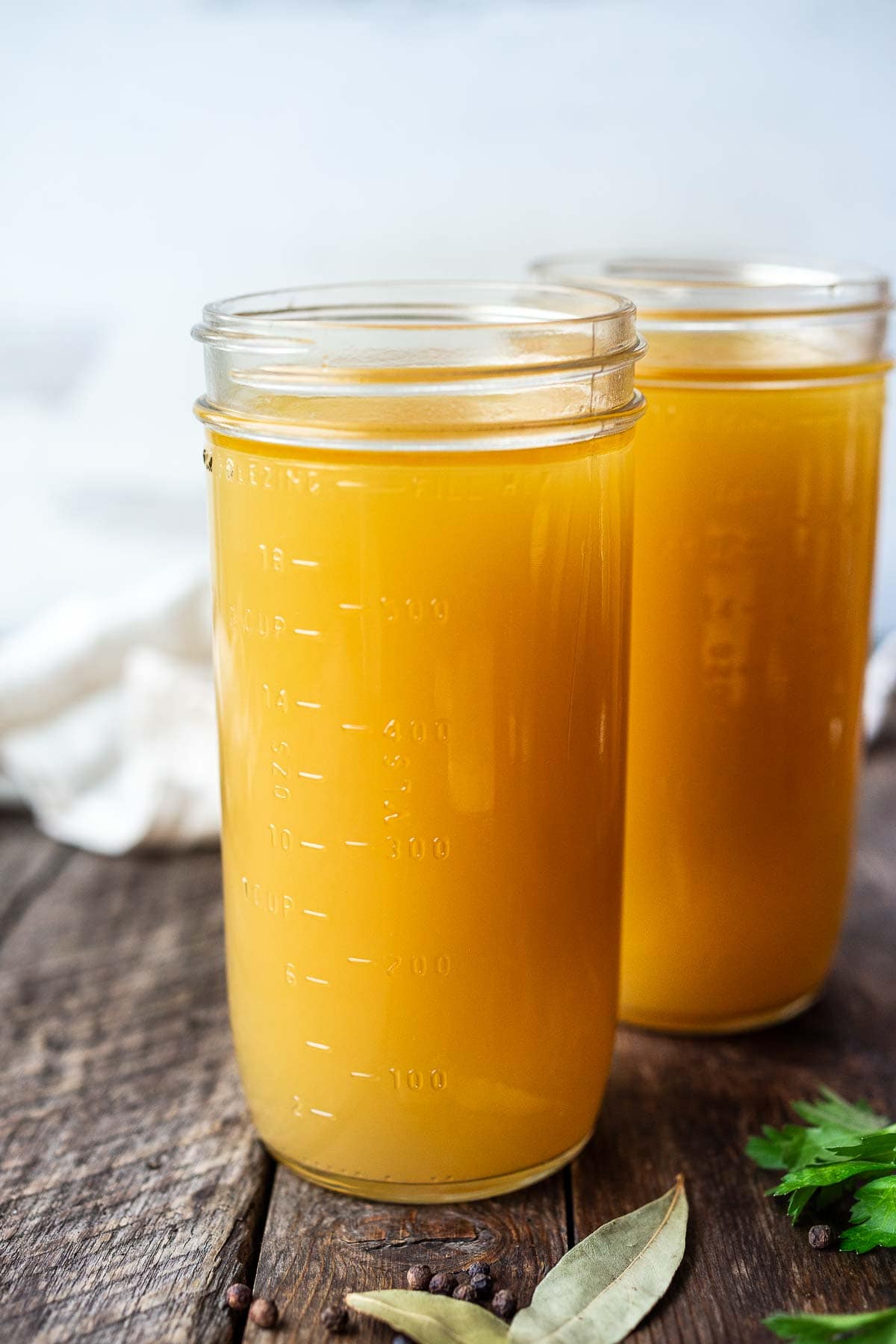 two mason jars filled with homemade chicken stock on wood surface. 