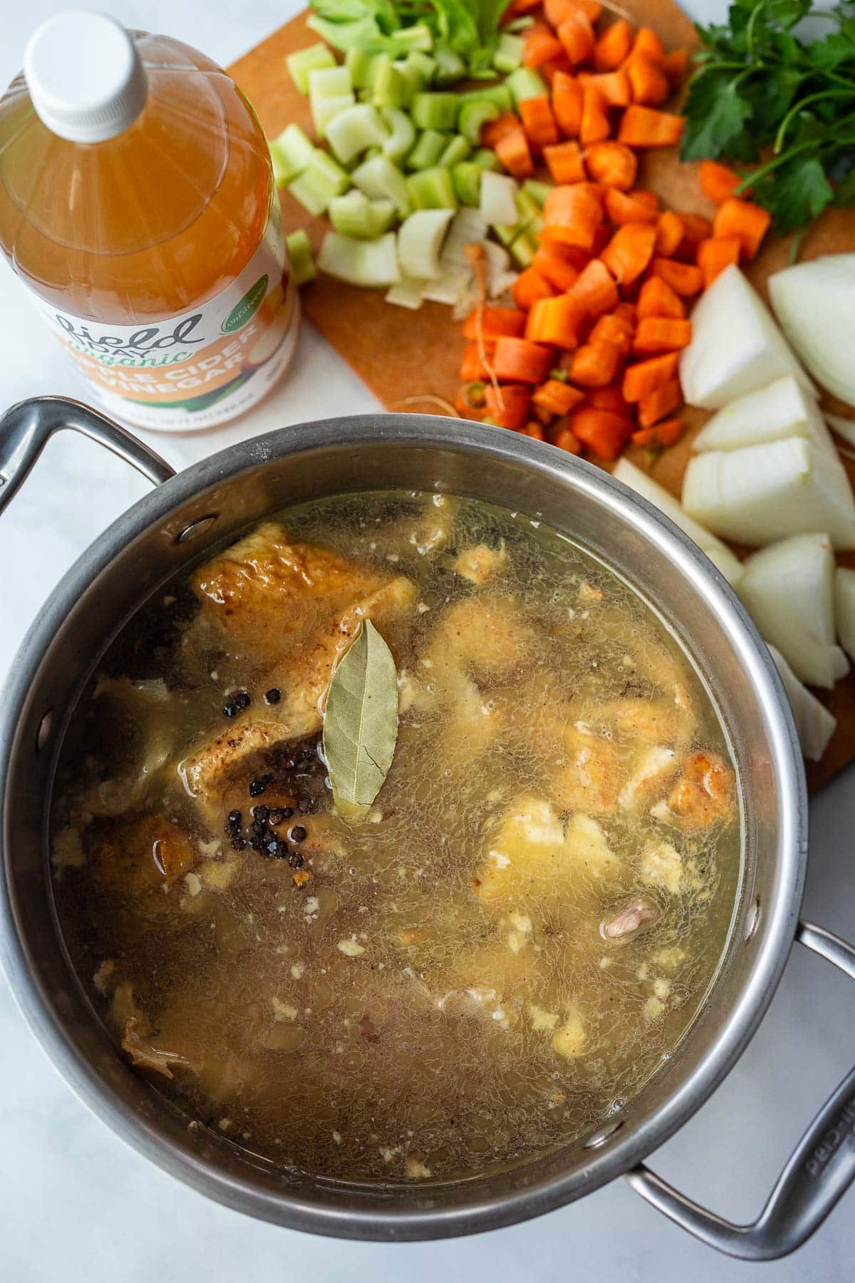 large stock pot with chicken stock topped with bay leaf and peppercorns. 