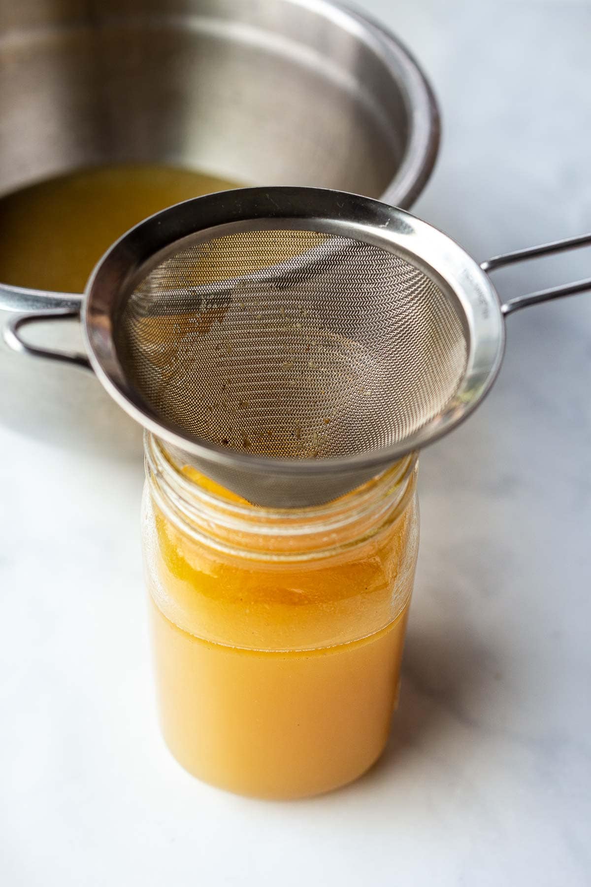 fine mesh strainer over mason jar filled with chicken stock. 