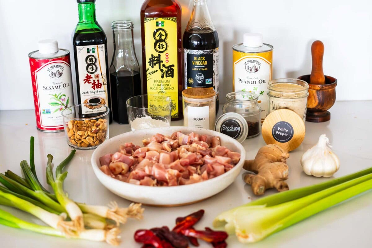ingredients for kung pao chicken laid out- bowl of cubed chicken, scallions, celery, chiles, ginger, garlic, spices, sugar, cornstarch, peanuts, oils and sauces.