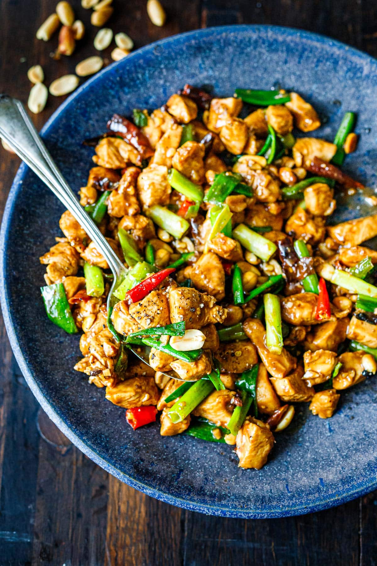 kung pao chicken in bowl with spoon with saucy chicken and stir-fried chiles and green onions.