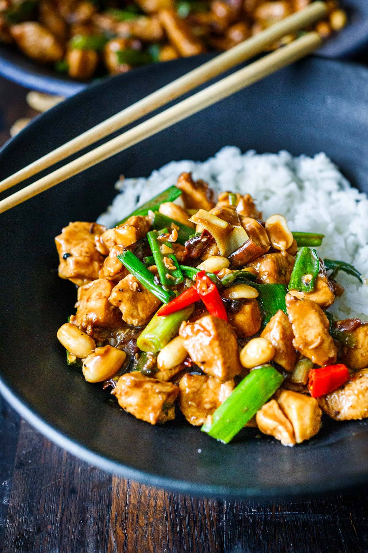 bowl of kung pao chicken served over steamed jasmine rice with chopsticks.