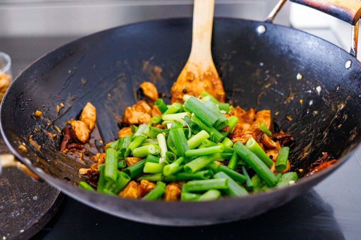 kung pao chicken cooking in wok with scallions added on top.