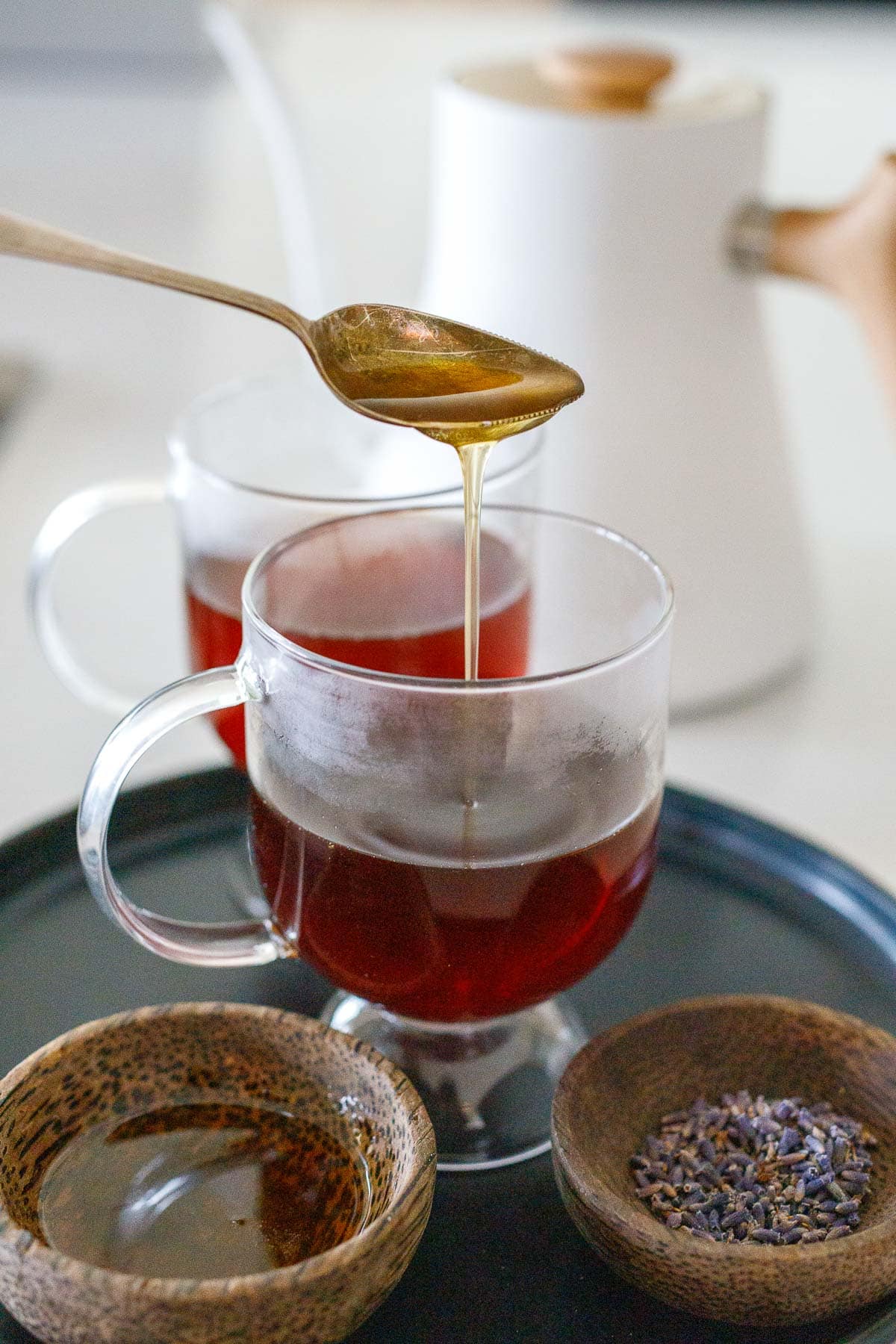 spoon dripping lavender honey vanilla simple syrup into glass mug with earl grey tea. 