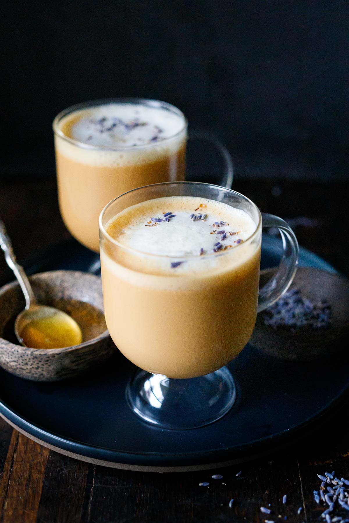 london fog latte in glass mugs garnished with dried lavender next to small bowl with simple syrup and spoon.