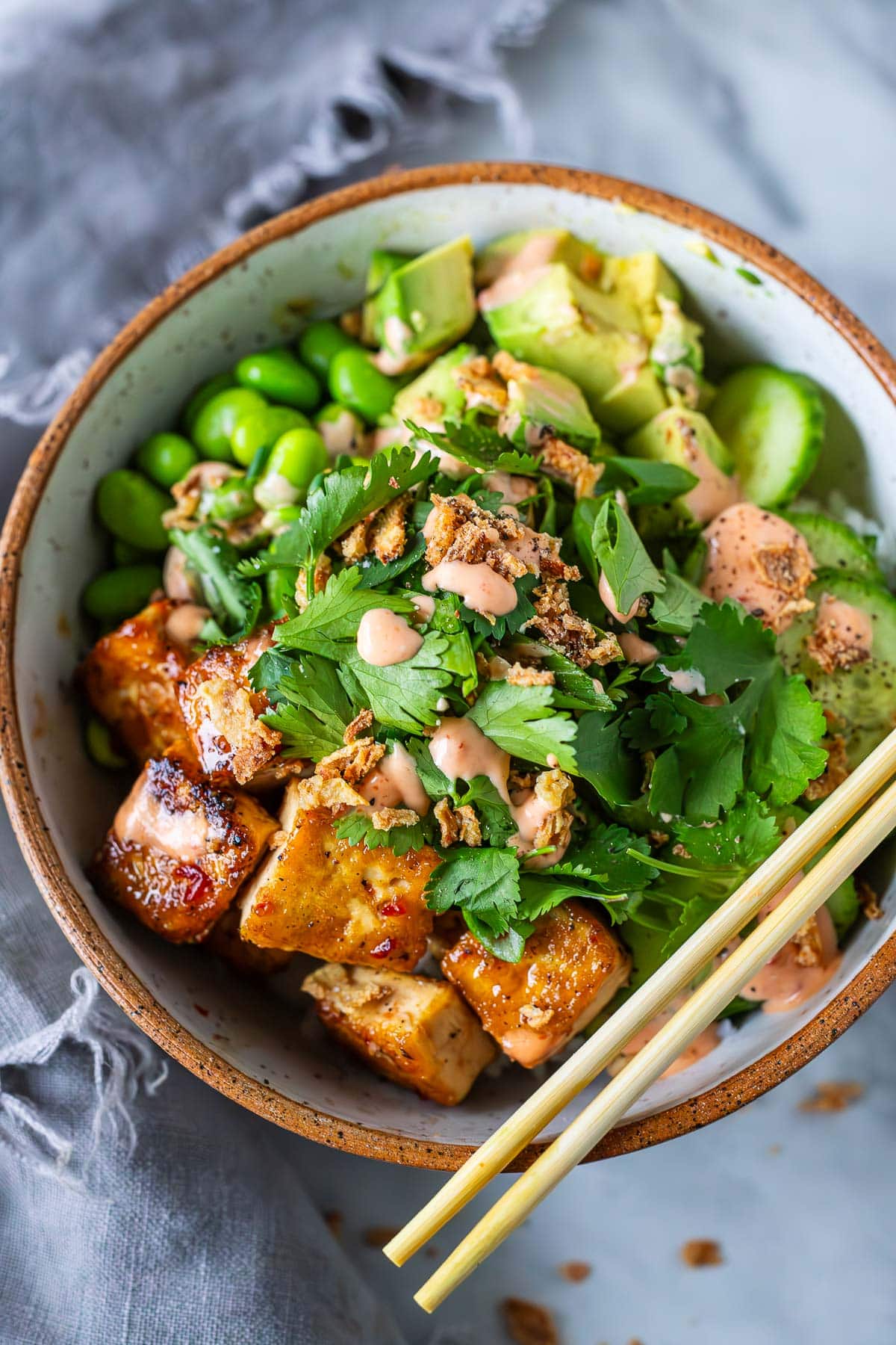tofu bowl topped with edamame, avocado, cucumber, cilantro, and crispy onions drizzled with yum yum sauce.