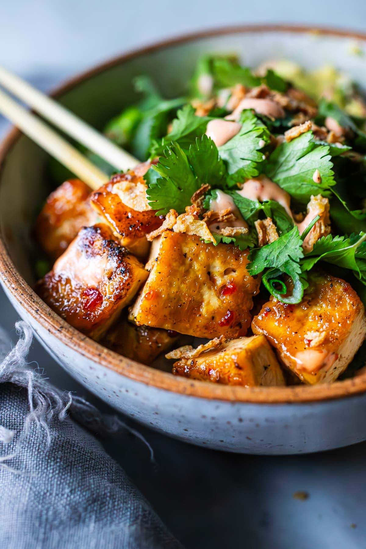 sticky glazed tofu bowl topped with cilantro, crispy onions, and yum yum sauce, in bowl with chopsticks.