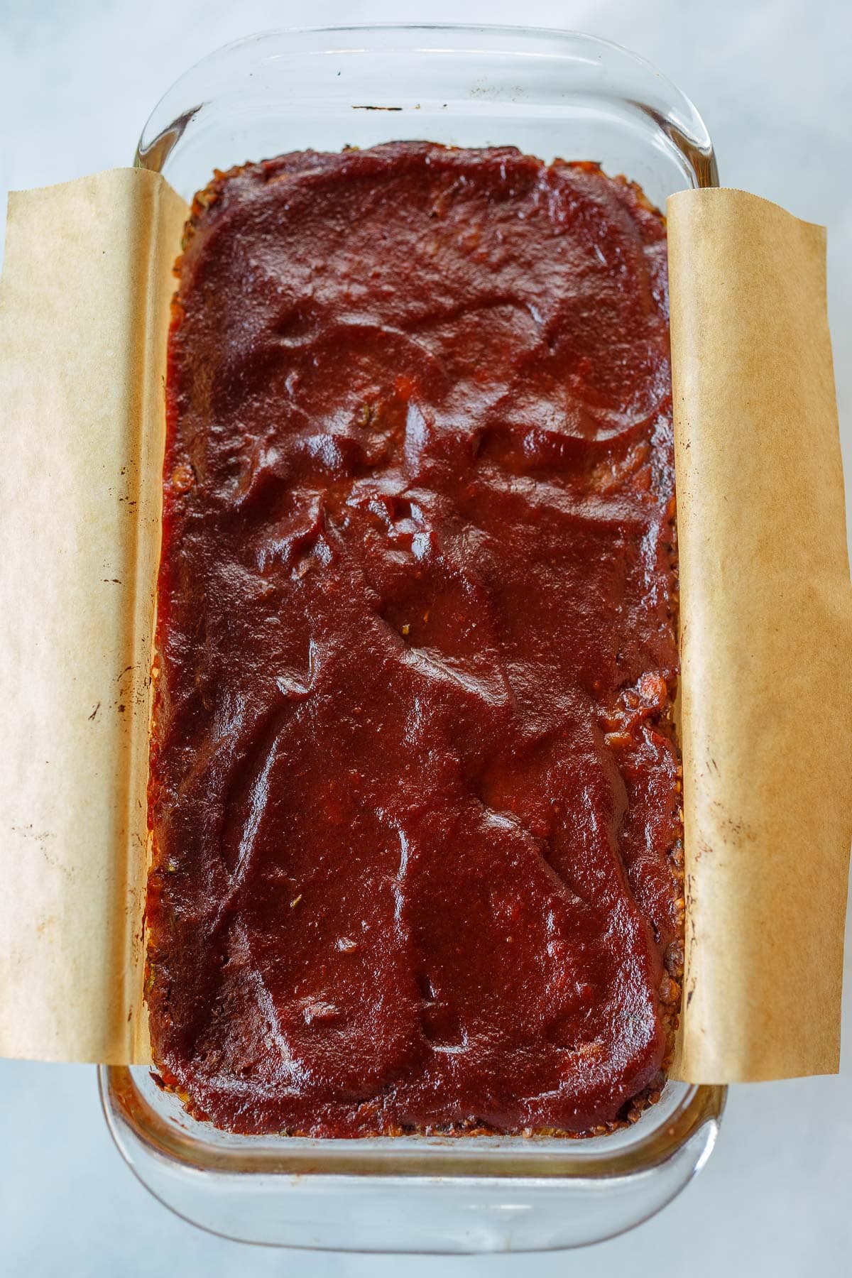 vegan meatloaf with glaze in loaf pan with parchment.