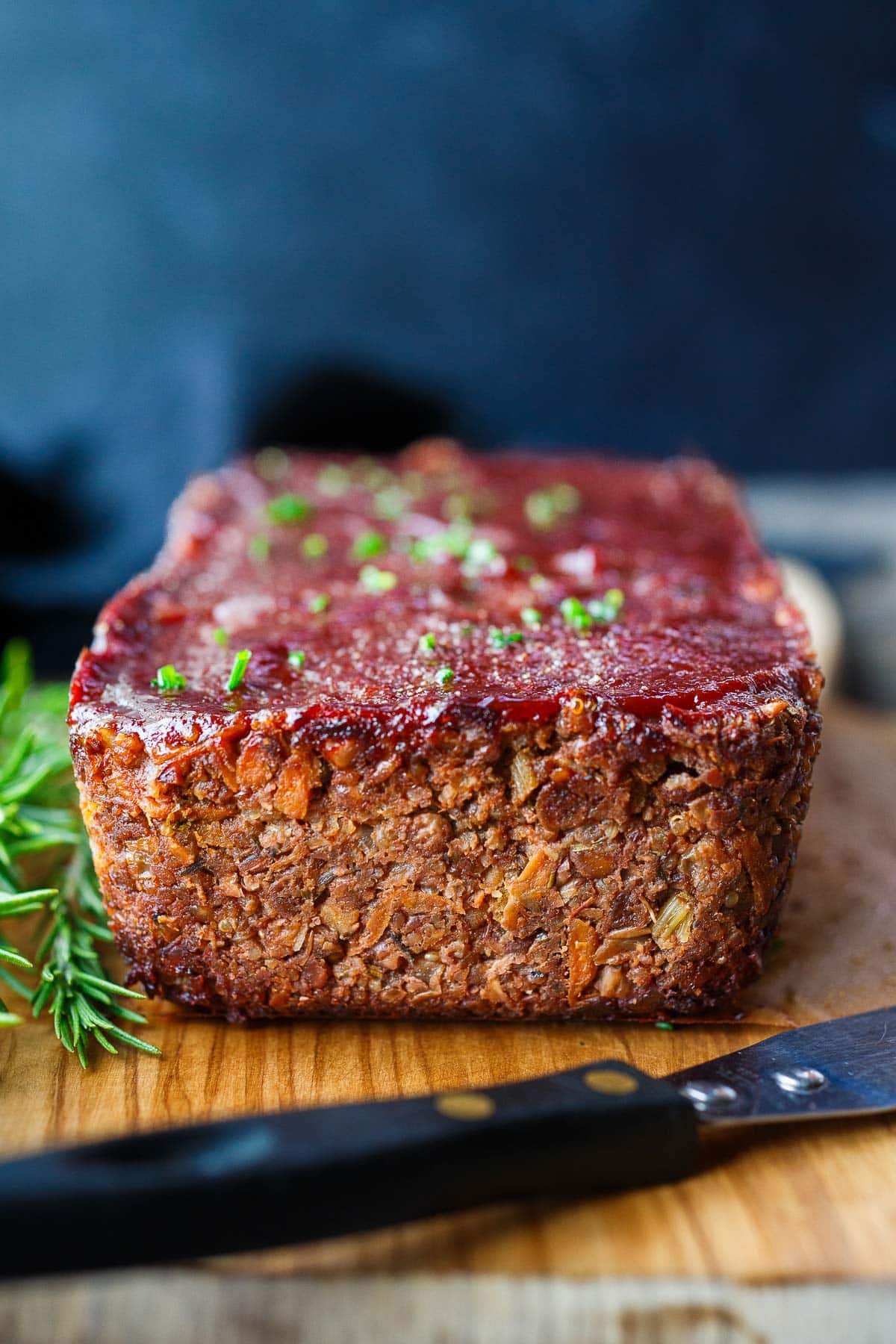 cooked vegan meatloaf with glaze on wood serving board with knife.