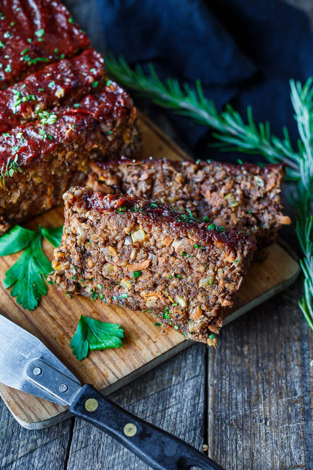 sliced vegan meatloaf on wood board with lentil veggie interior and glaze on top with fresh parsley garnish.