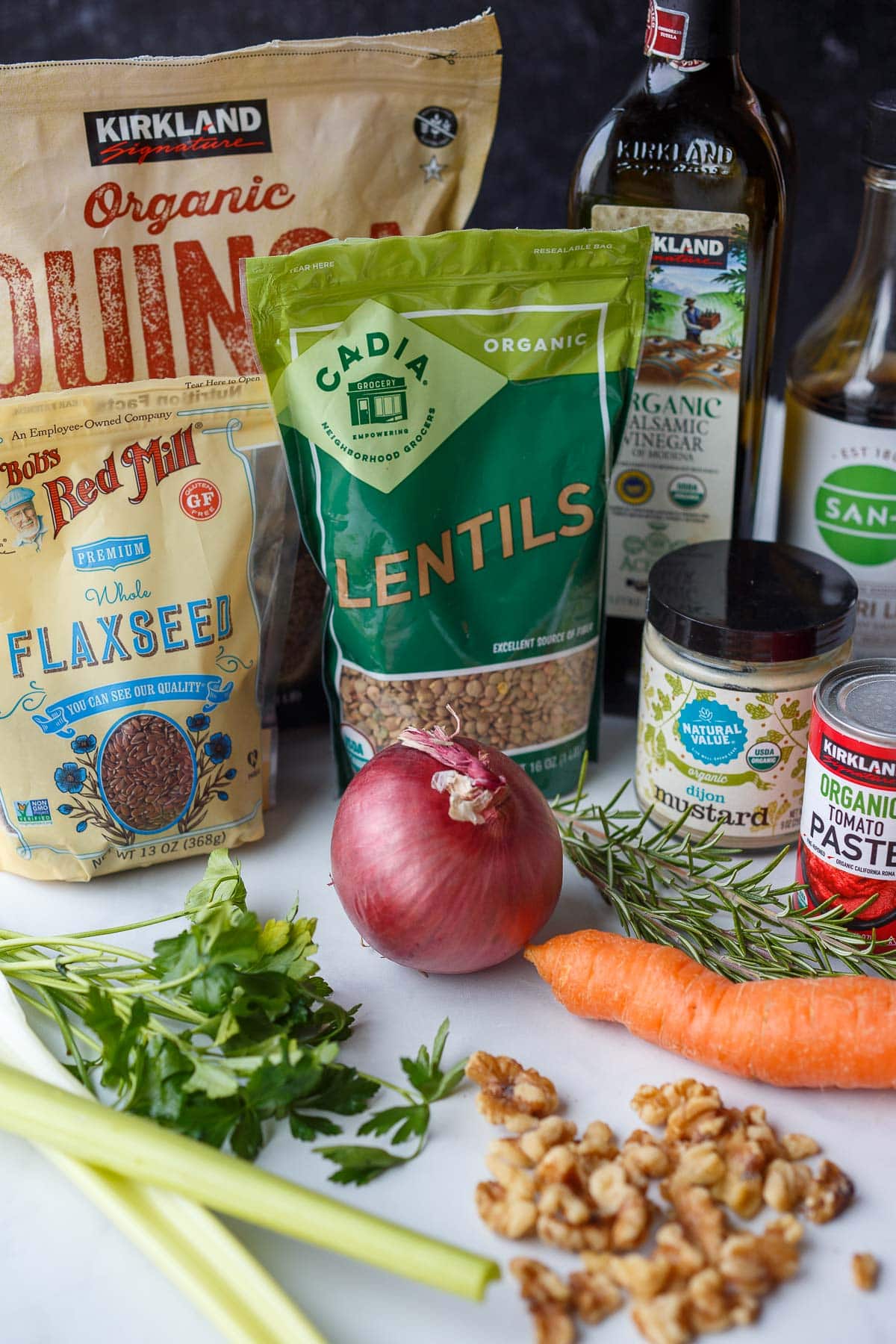 ingredients laid out for vegan meatloaf recipe - flaxseed, lentils, quinoa, balsamic, tamari, dijon, tomato paste, rosemary, parsley, onion, carrot, walnuts, celery.