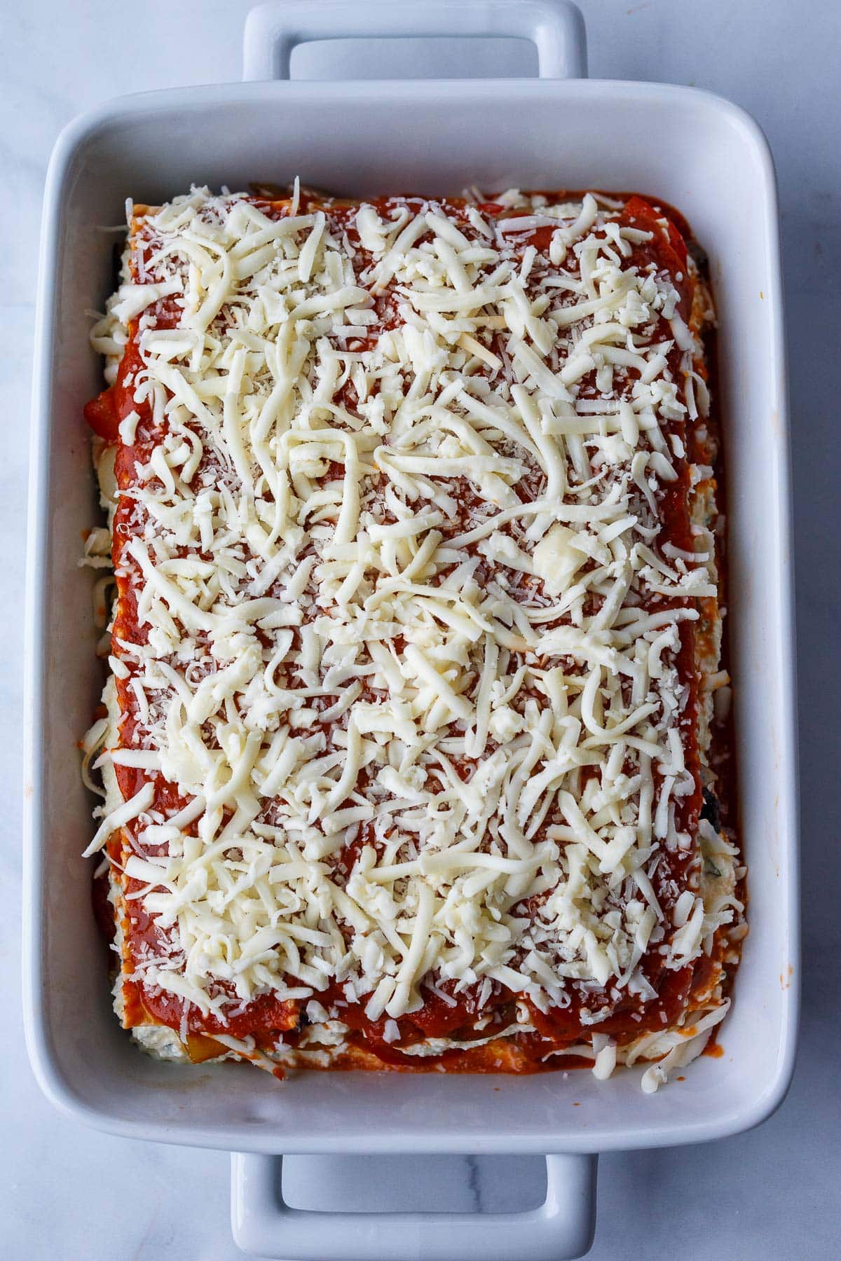 top layer of unbaked lasagna with grated mozzarella over marinara layer.