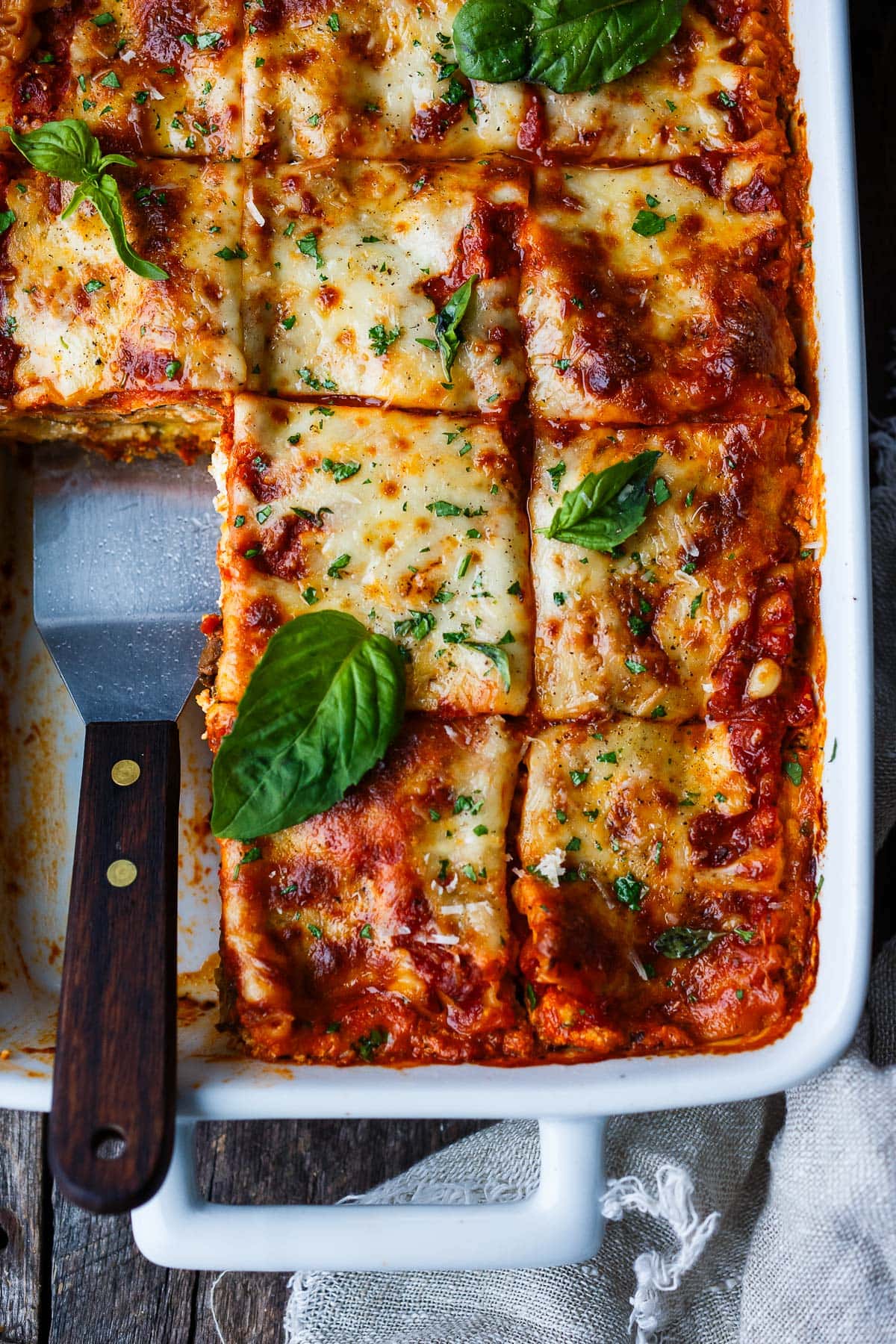 baking dish of vegetable lasagna with spatula in pan to scoop out a piece.