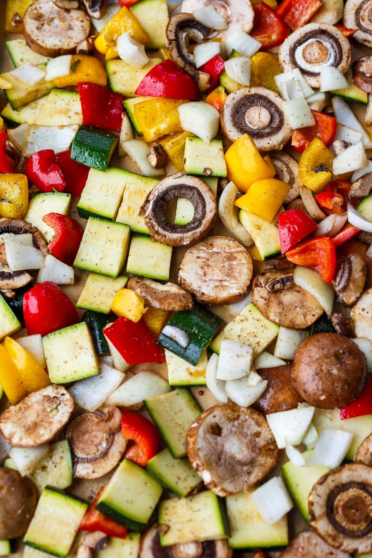 chopped veggies on baking sheet seasoned with oil, salt, and pepper - mushrooms, zucchini, onion, and peppers.
