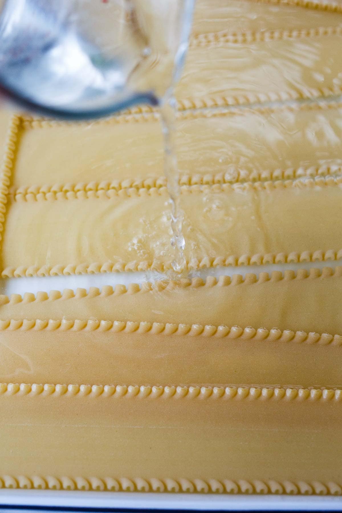 baking sheet with uncooked lasagna noodles laid out and pouring hot water over top.
