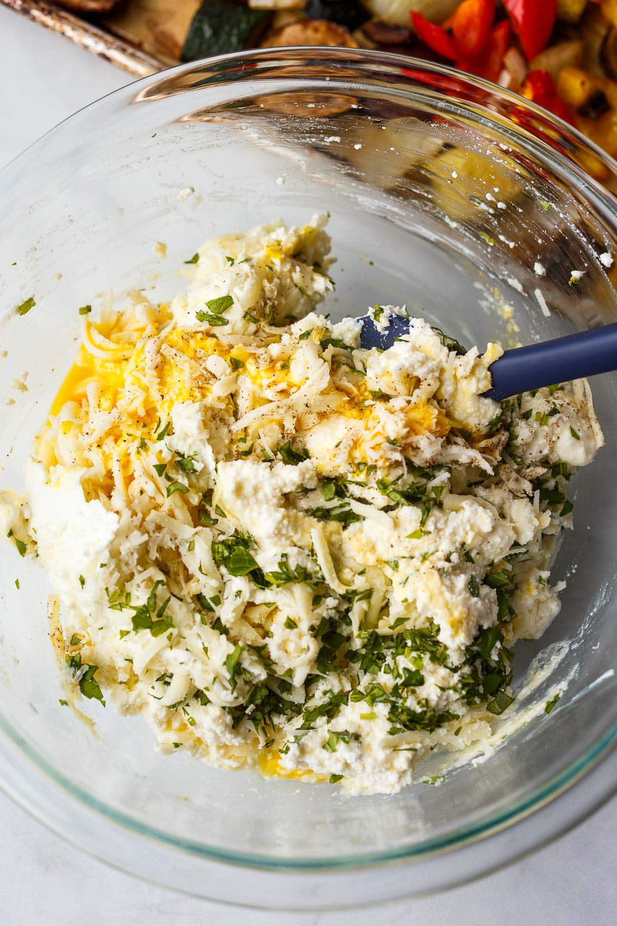 glass mixing bowl with spatula mixing the ricotta mixture together with fresh basil.