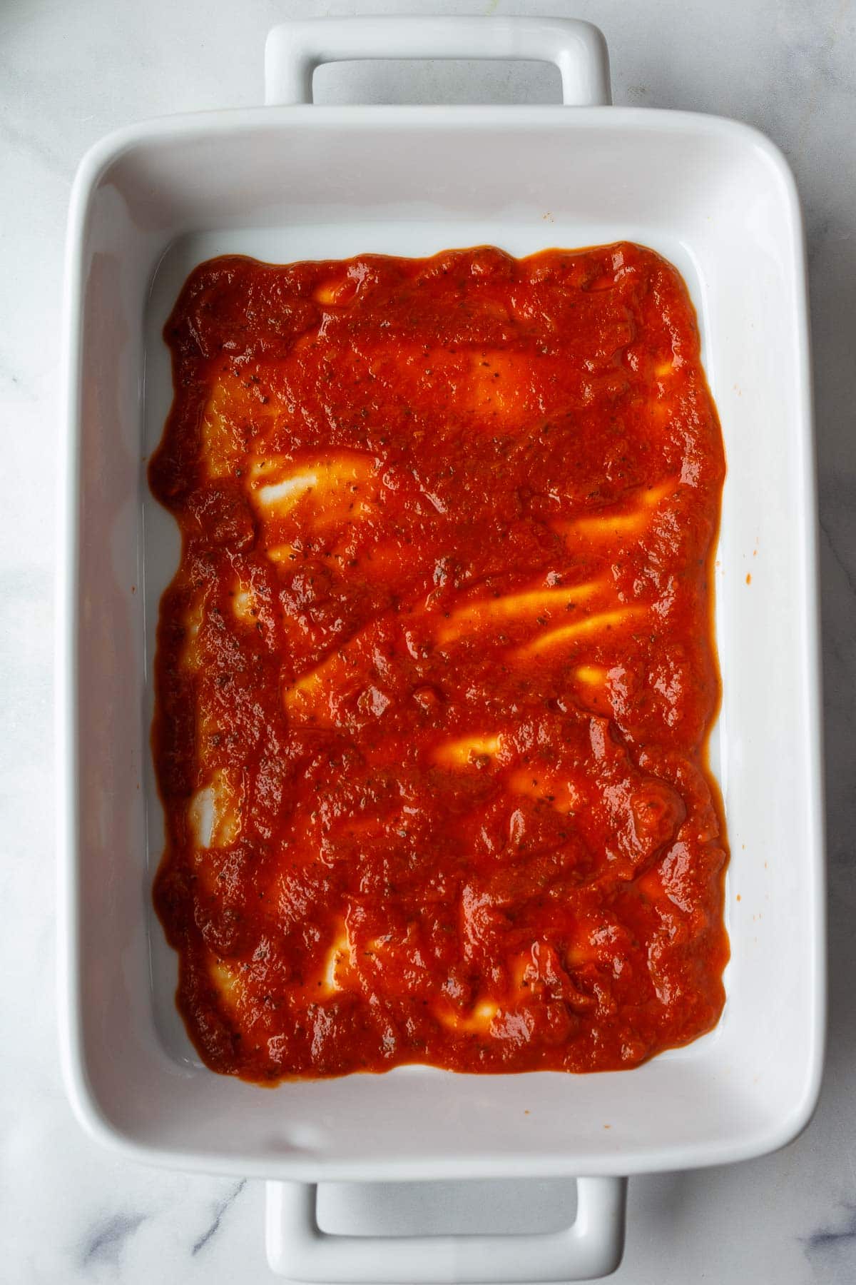 casserole dish with marinara spread across bottom.