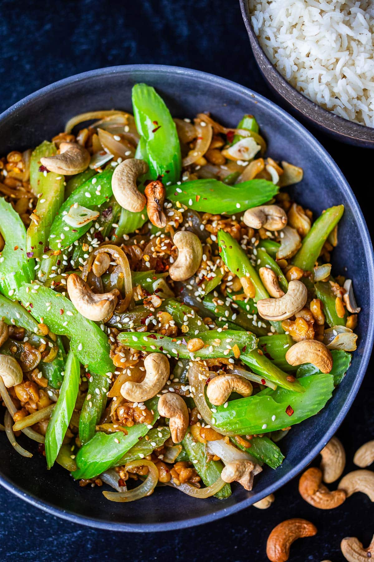 bowl of celery stirfry with cashews, sesame seeds, and red pepper flakes for garnish.