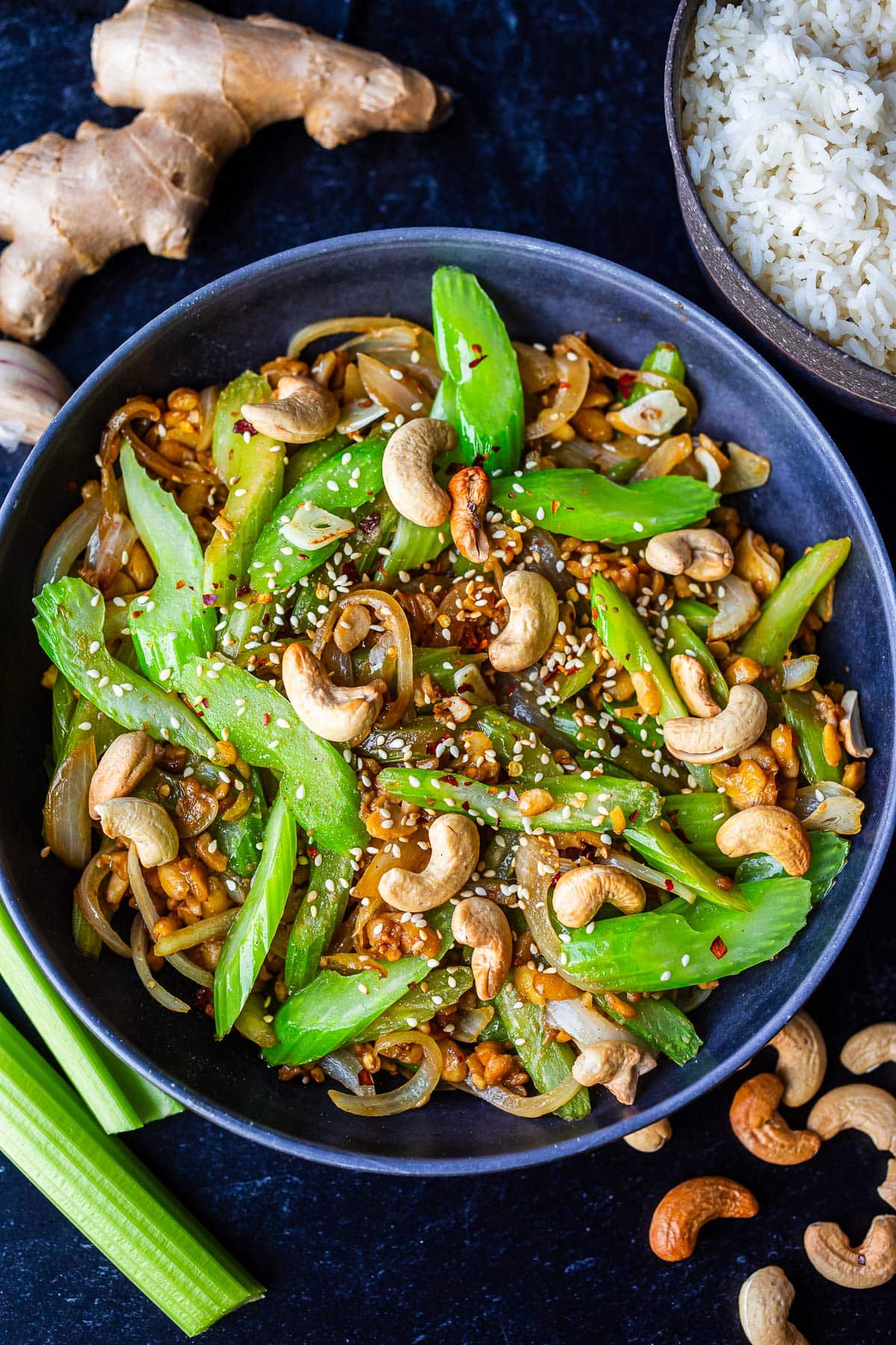 blue serving bowl with celery stirfry topped with cashews, red pepper flakes, and sesame seeds. 
